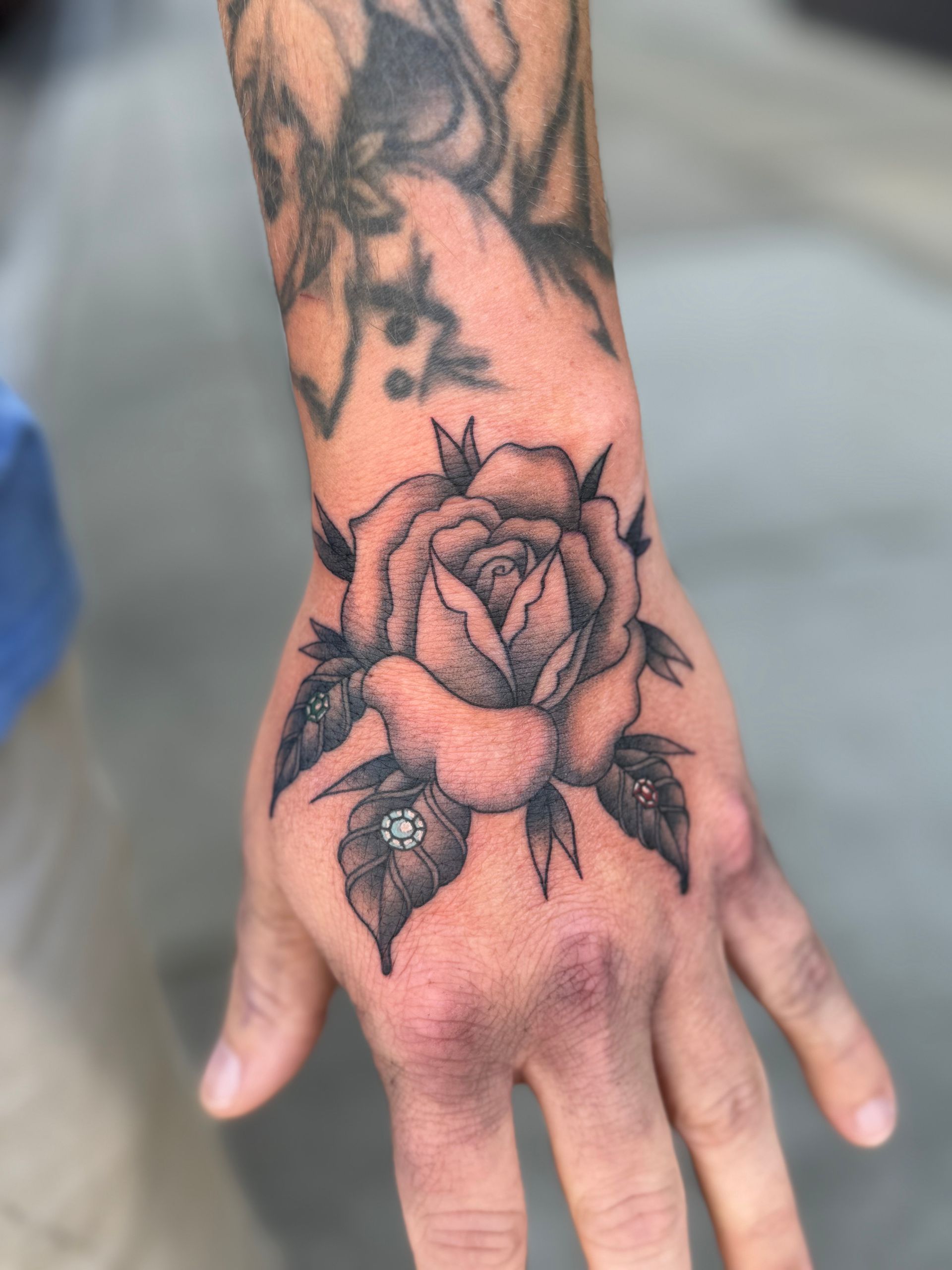 Hand with black floral tattoo on the back and forearm, resting on a gray surface