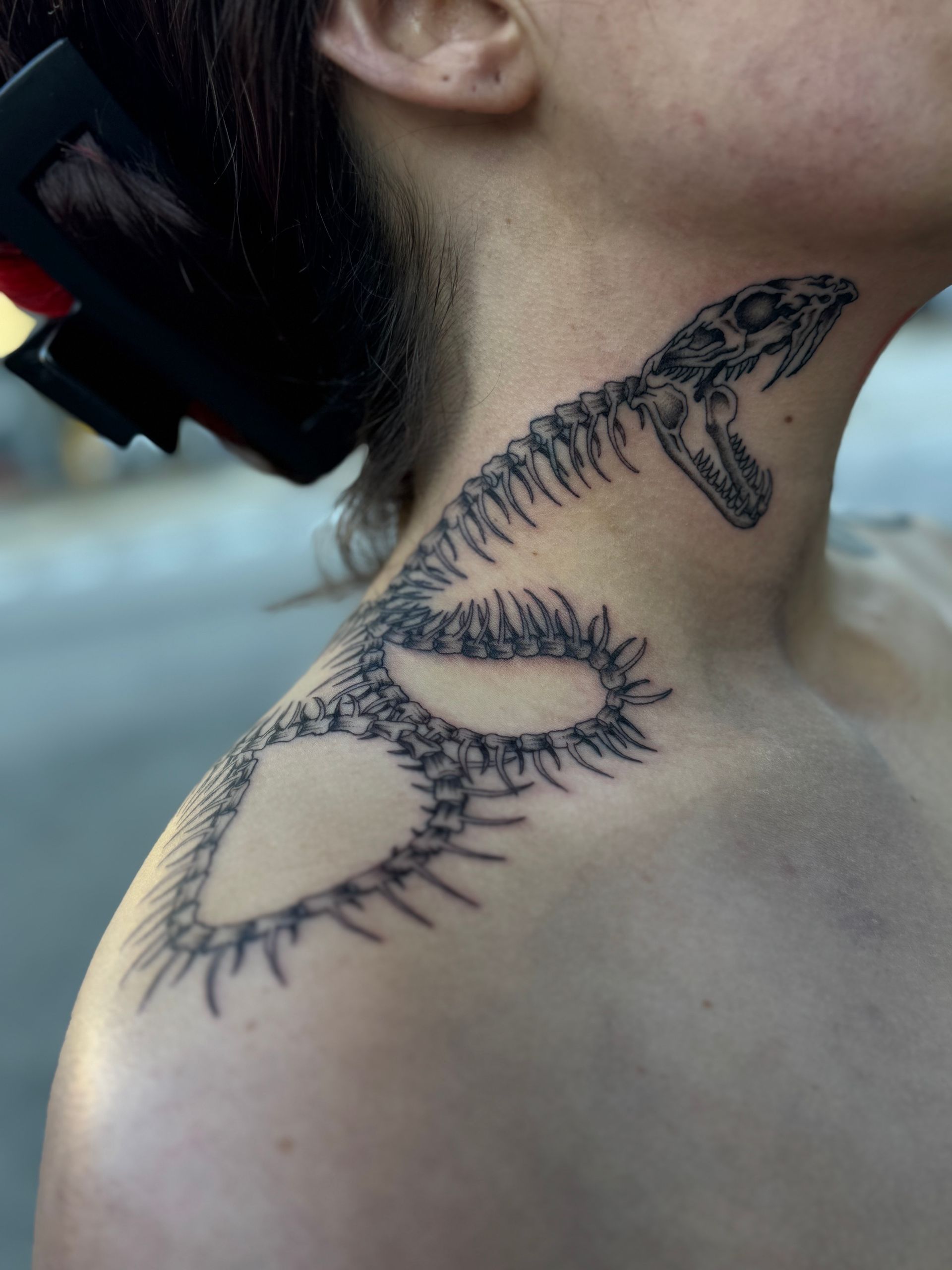 Close-up of a neck and shoulder with a black linework snake tattoo wrapping around the skin.
