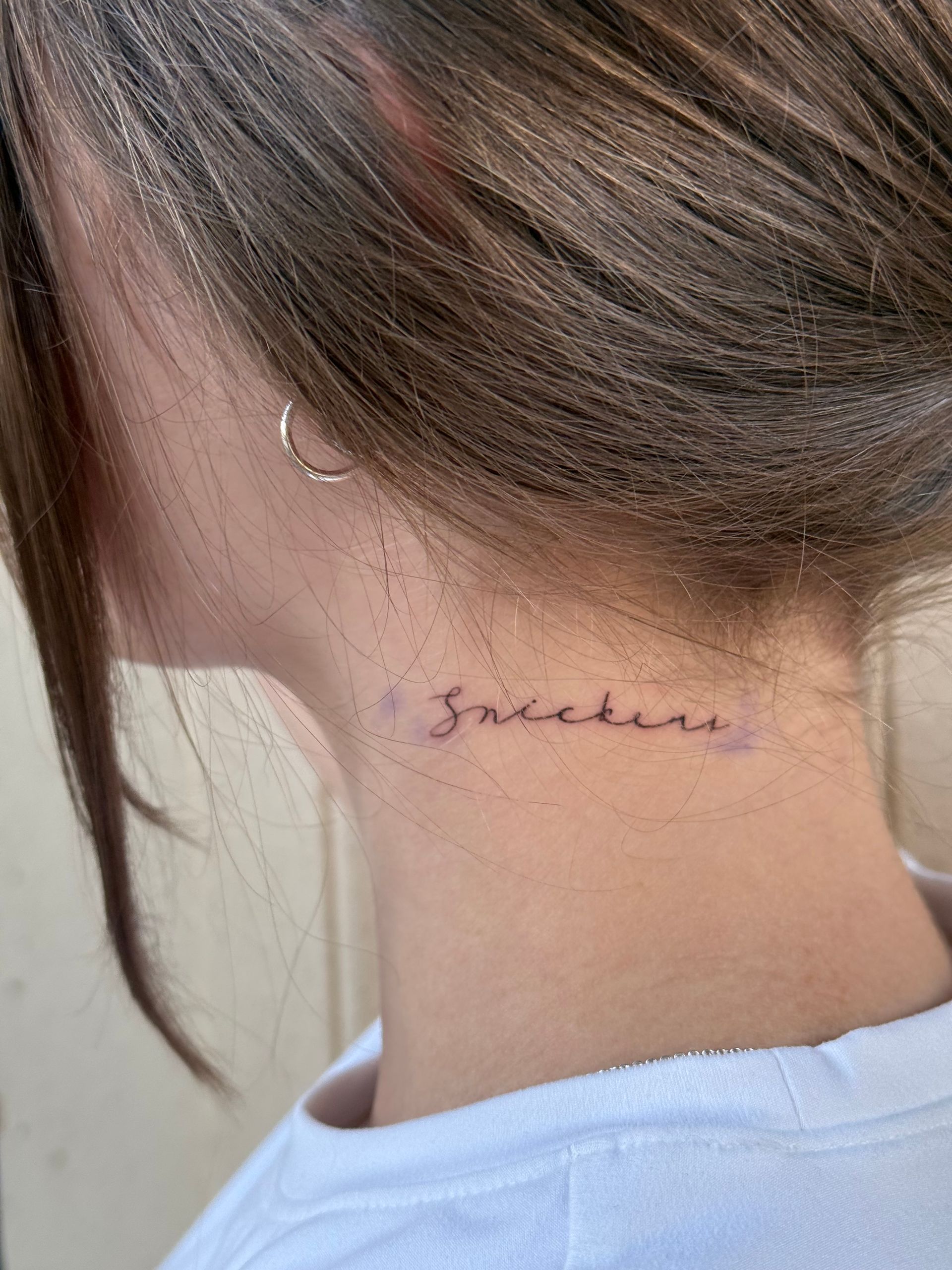 Back of a neck with a small cursive tattoo below the hairline.