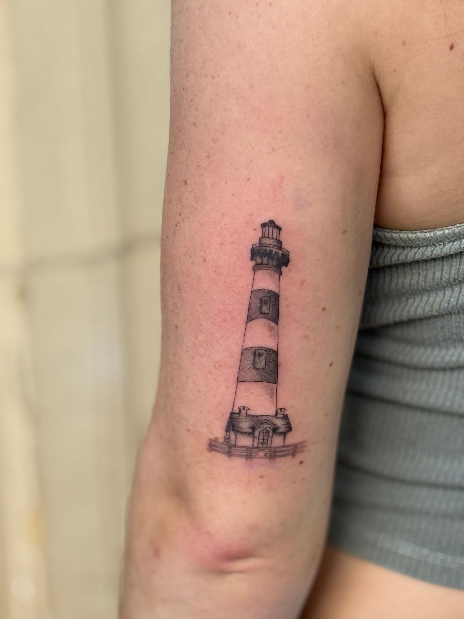 Close-up of an arm with a small lighthouse tattoo near the elbow.