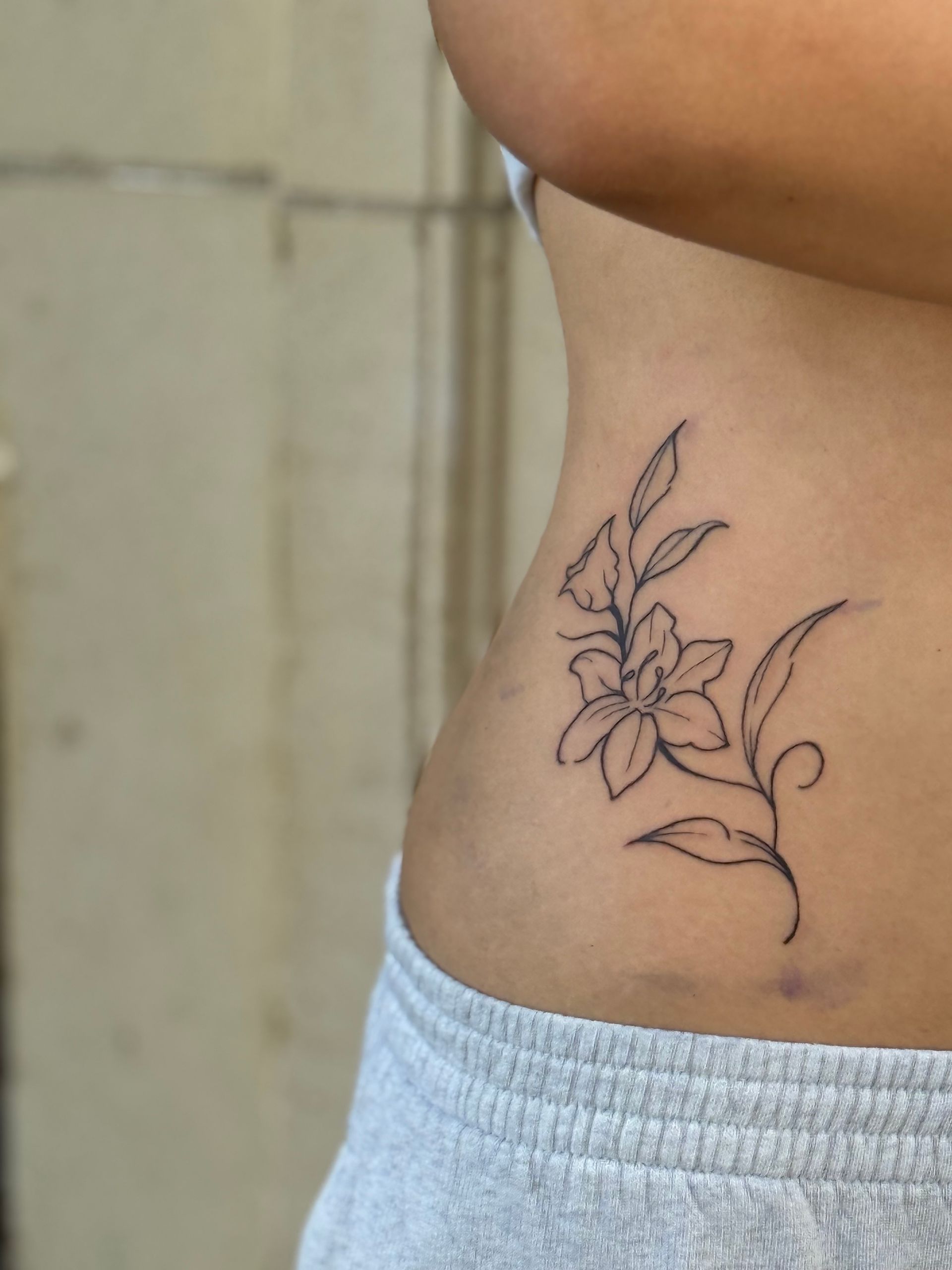 Small black floral tattoo on a person’s side abdomen above a gray waistband