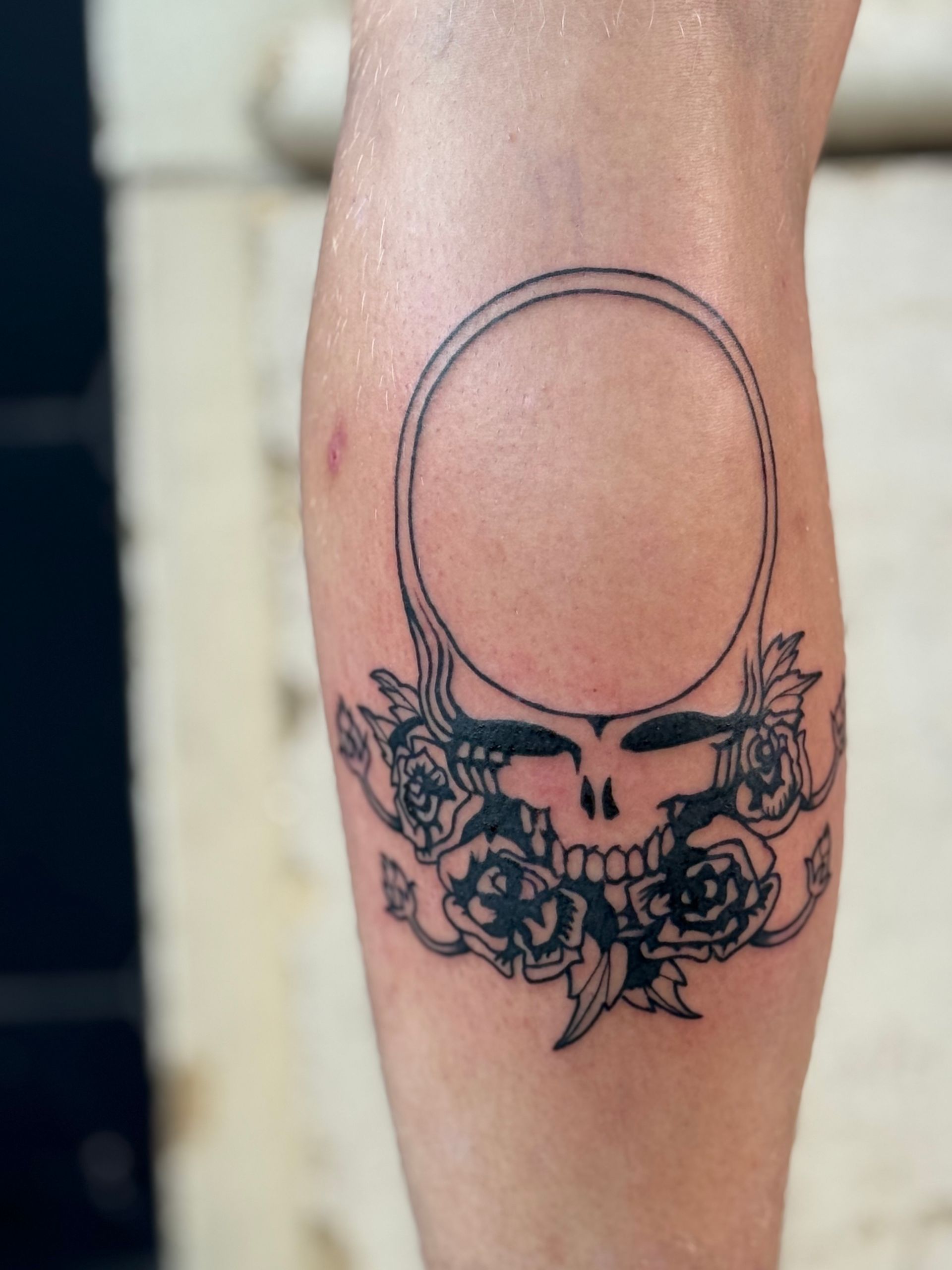 Close-up of a forearm tattoo featuring a skull with floral details and an empty circular outline above it