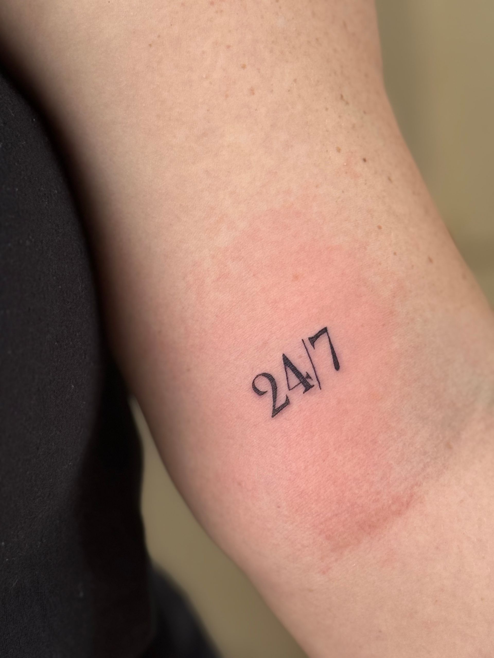 Close-up of a forearm with a small black 24/7 tattoo and a faint red mark nearby