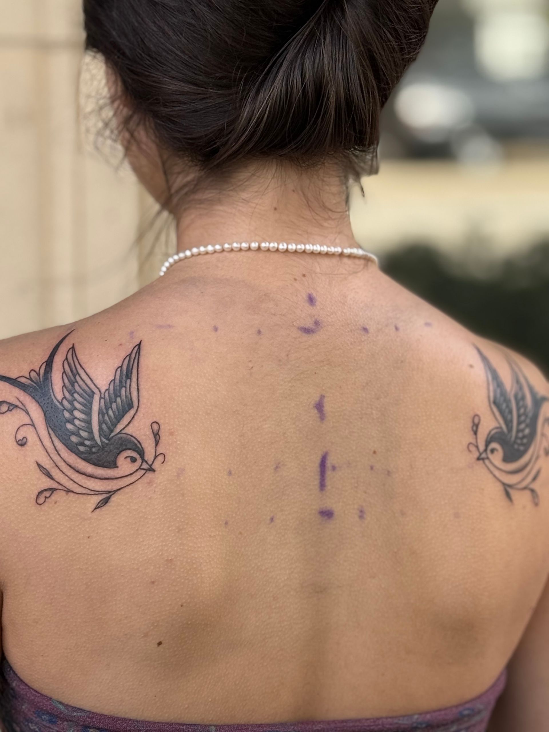 Back view of a woman’s upper back with butterfly tattoos and a vertical dotted purple line down the spine