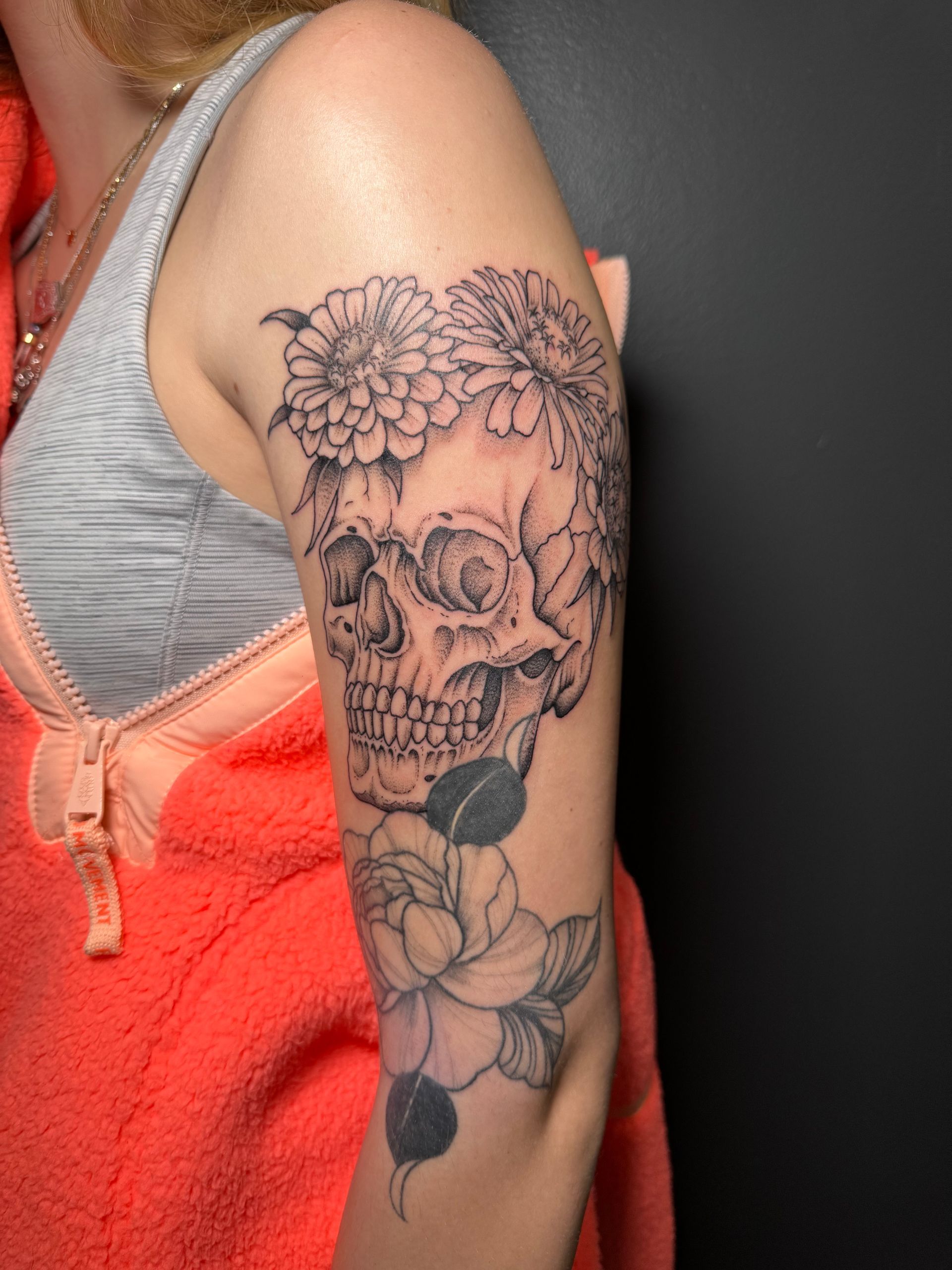 Side view of an arm with a black floral skull tattoo against a gray and orange top