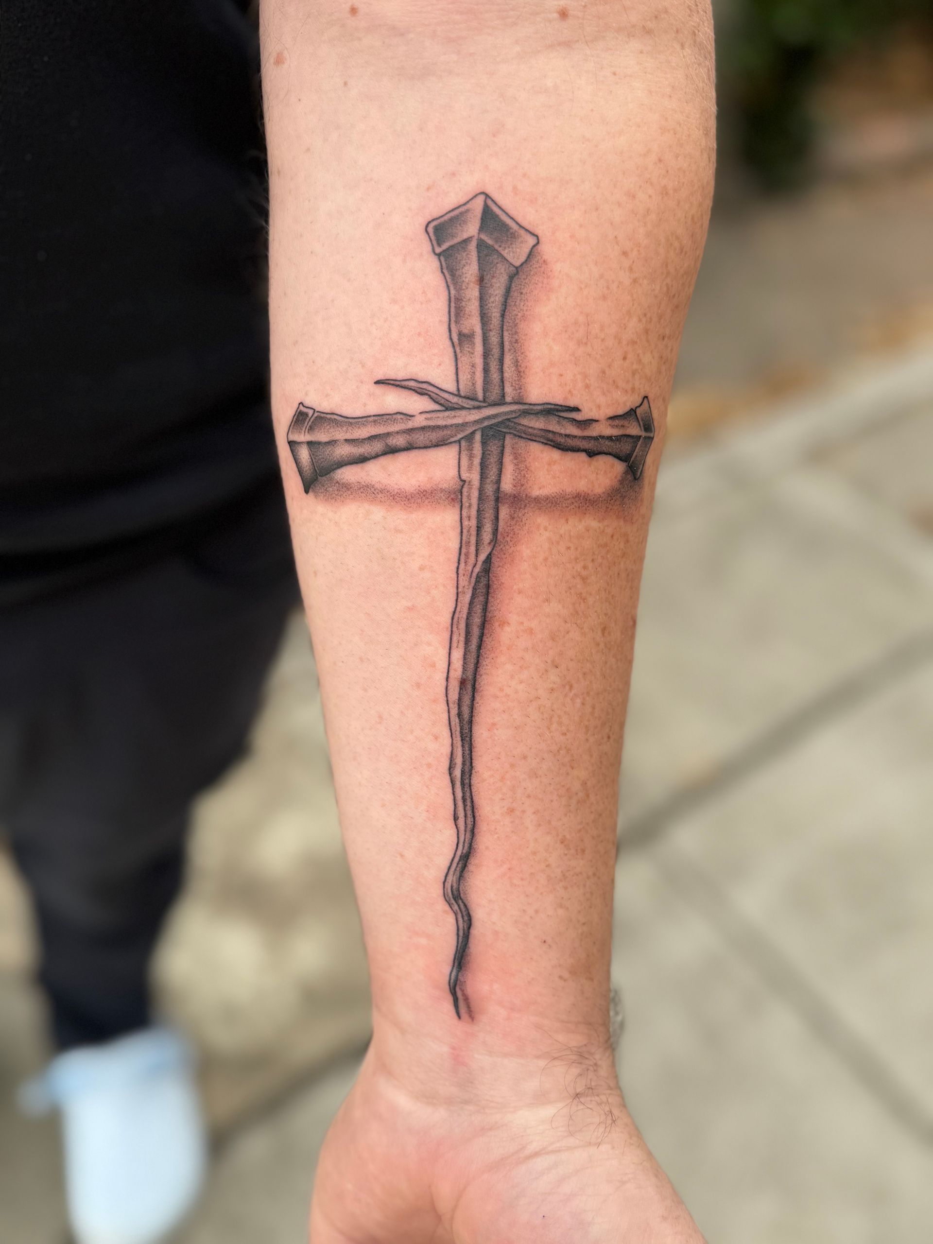 Black sword tattoo on a forearm against a light sidewalk background