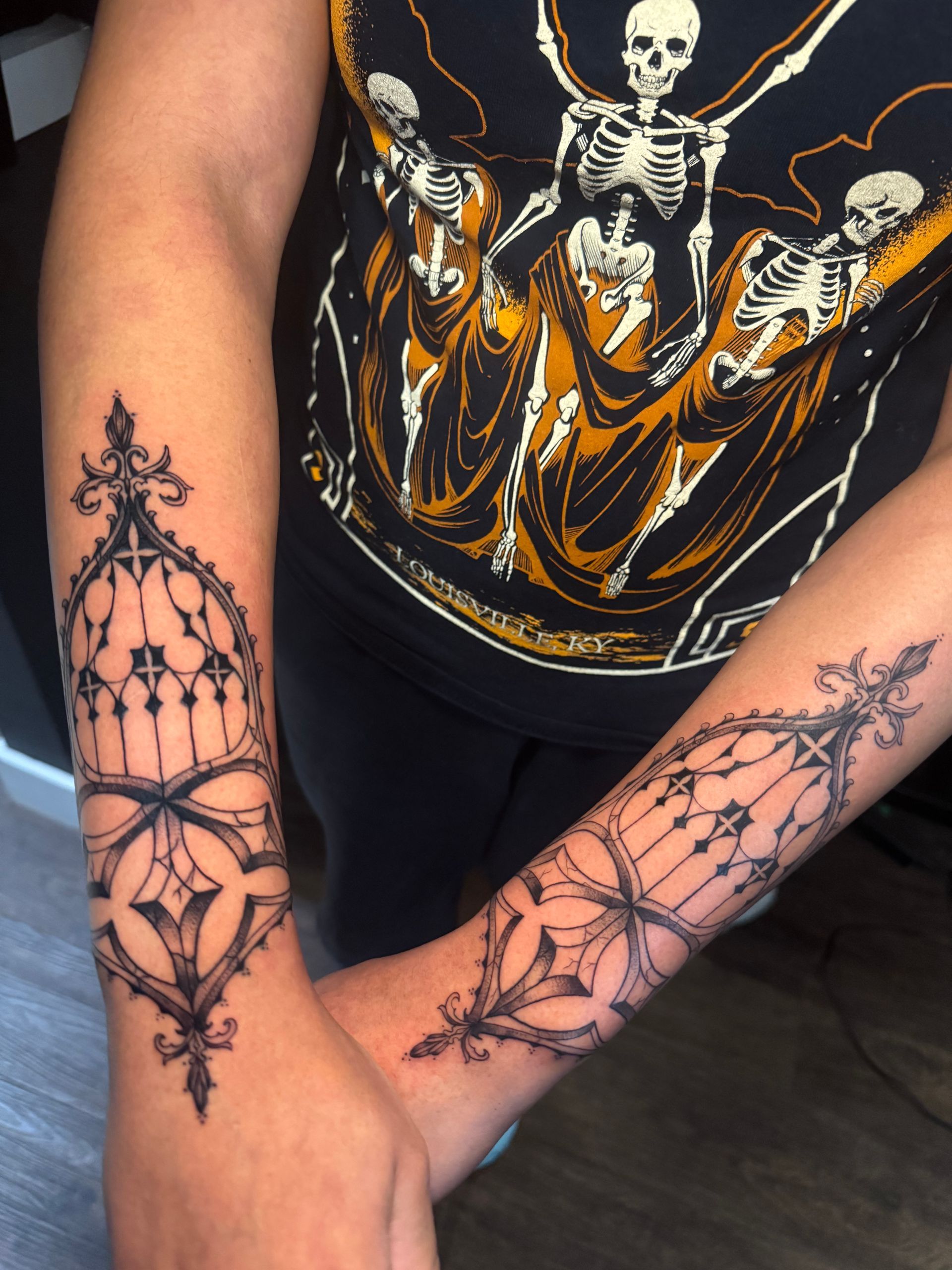 Arms with matching black lace-style tattoos, shown against a black graphic tank top.