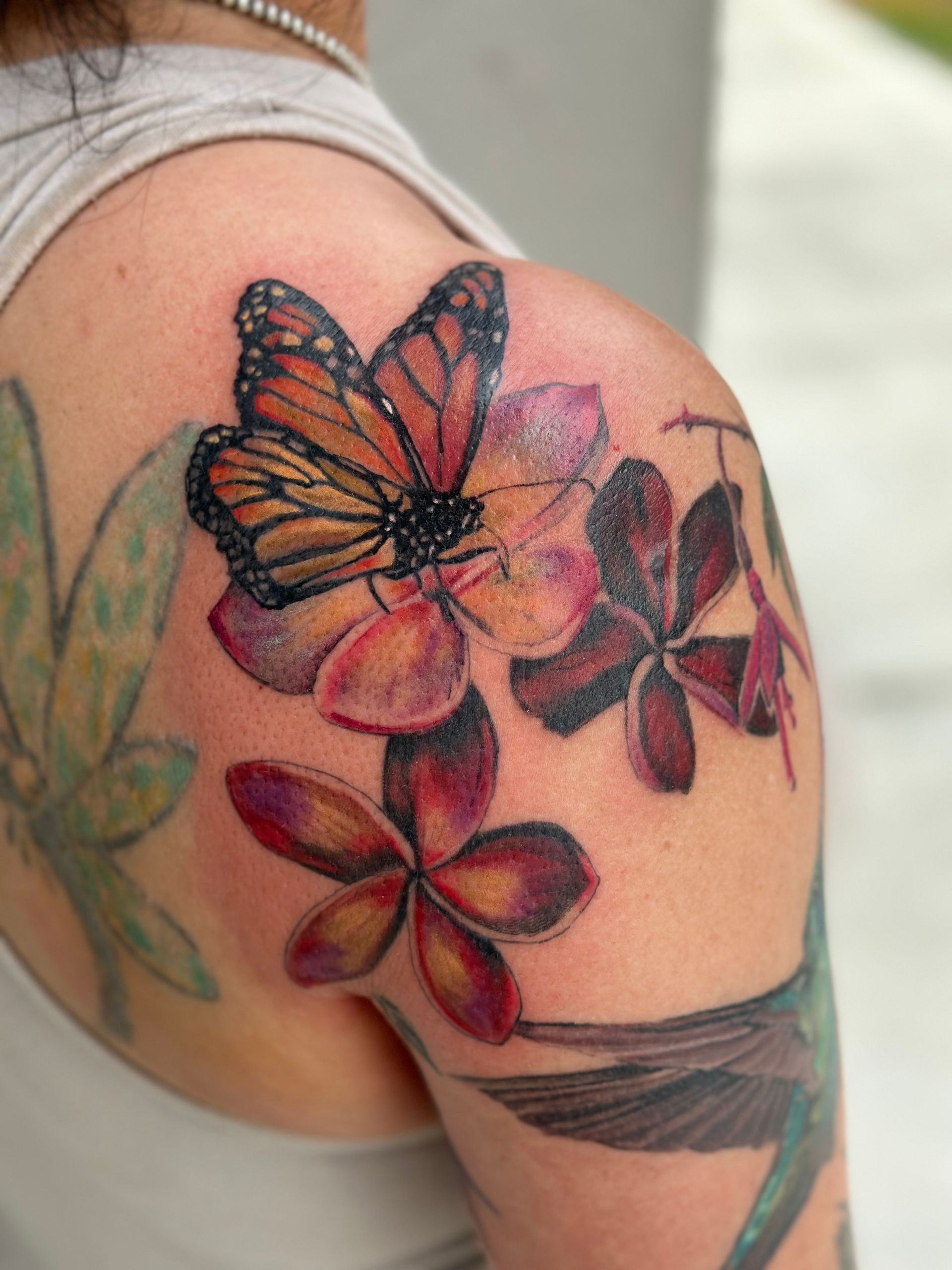 Butterfly tattoo on a shoulder with red and purple floral accents
