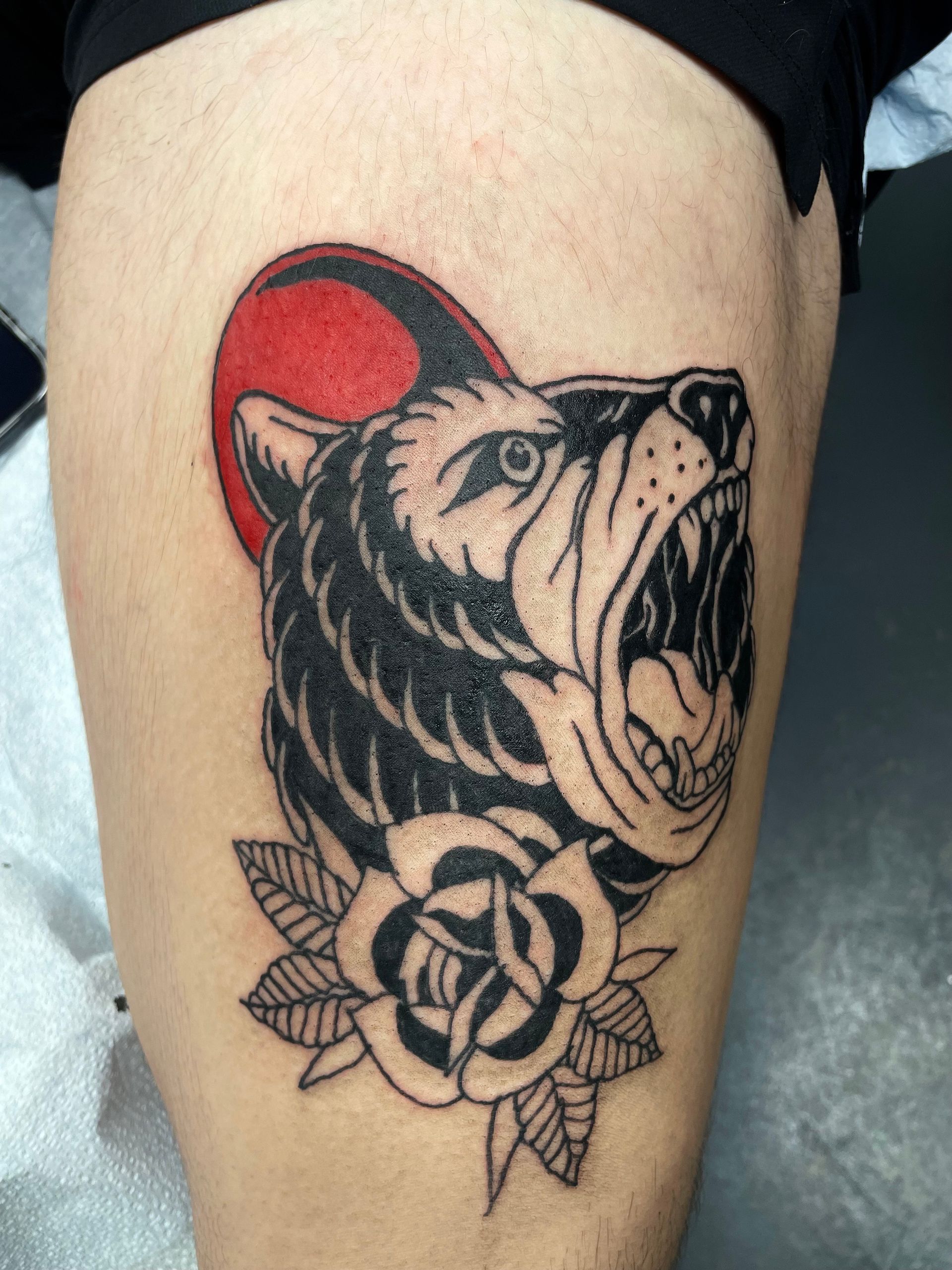 Tattoo of a roaring bear head with red sun and black rose on a leg