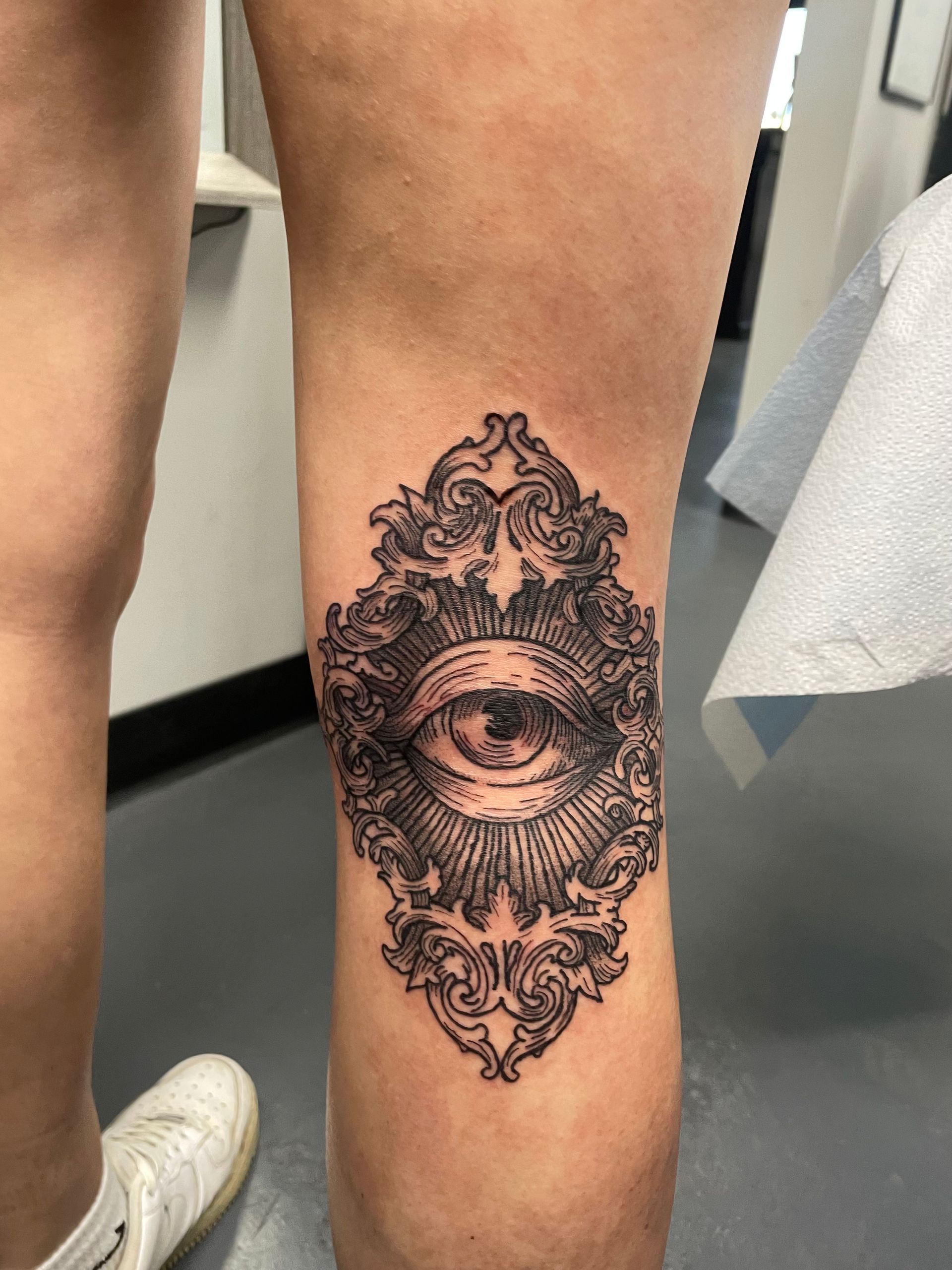 Intricate black eye tattoo on the side of a person’s calf, with ornate symmetrical detailing