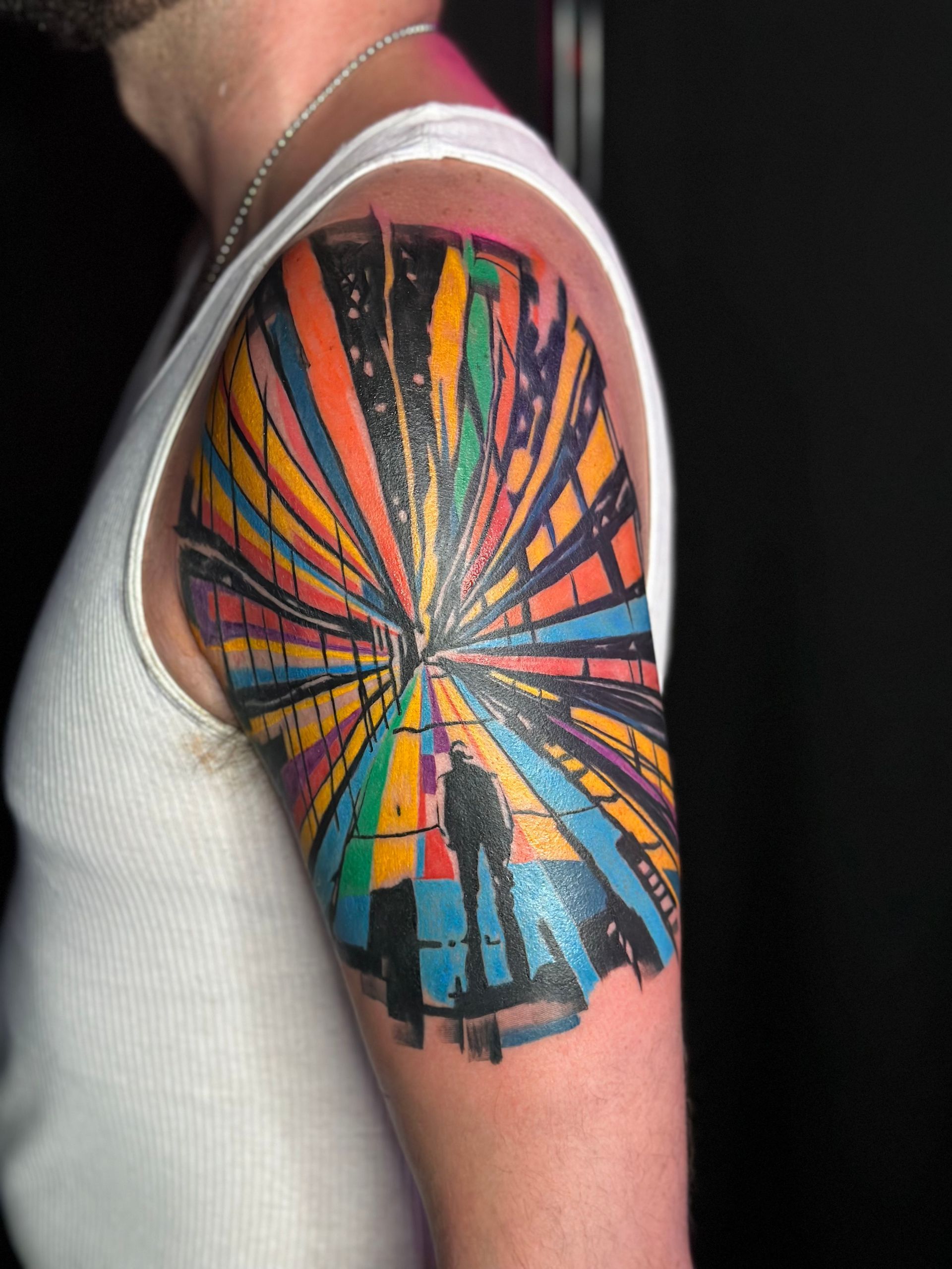 Arm tattoo with a colorful radial sunburst design on an upper arm in a white tank top