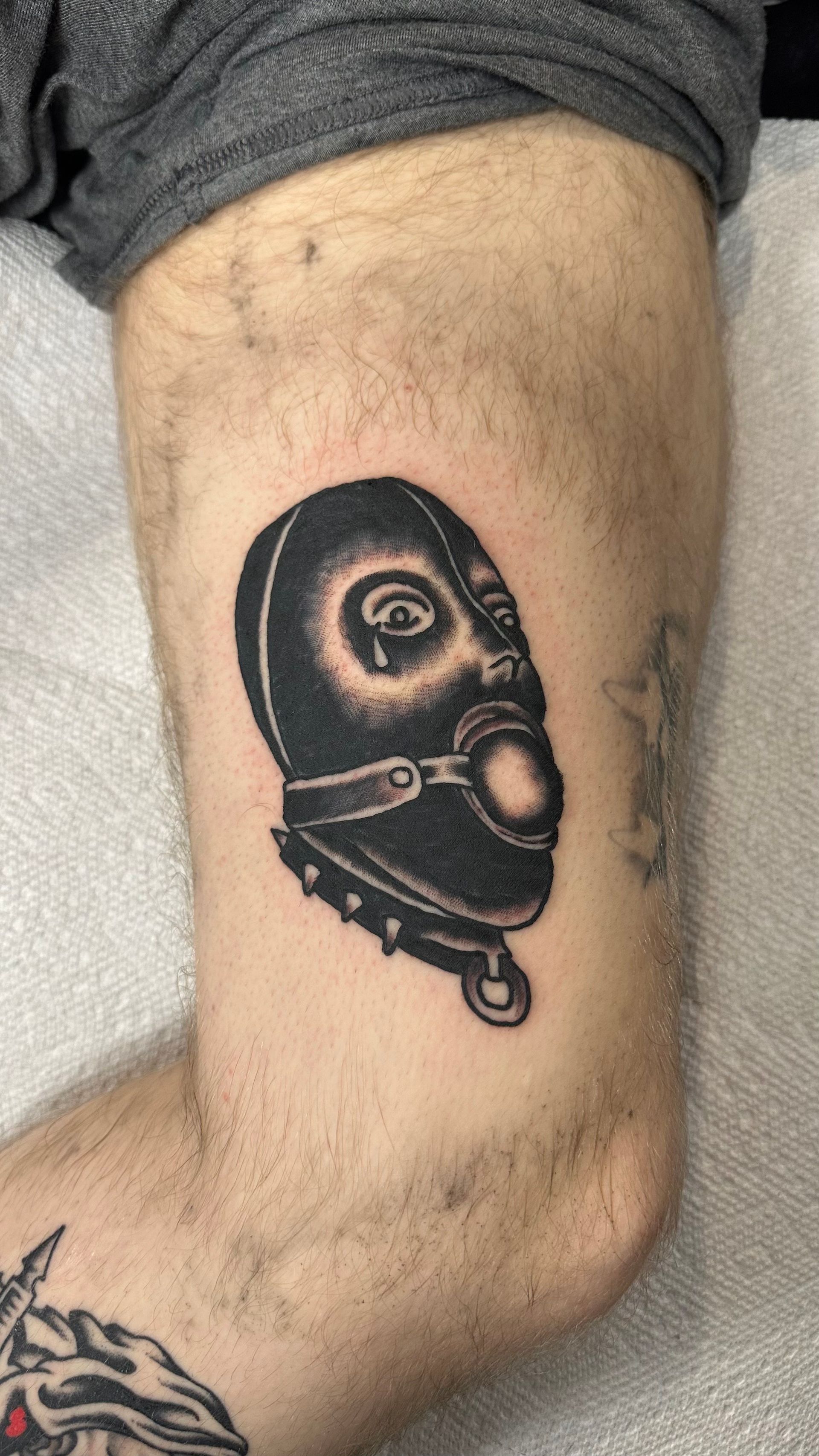 Close-up of a forearm with a black face-shaped tattoo near the elbow.