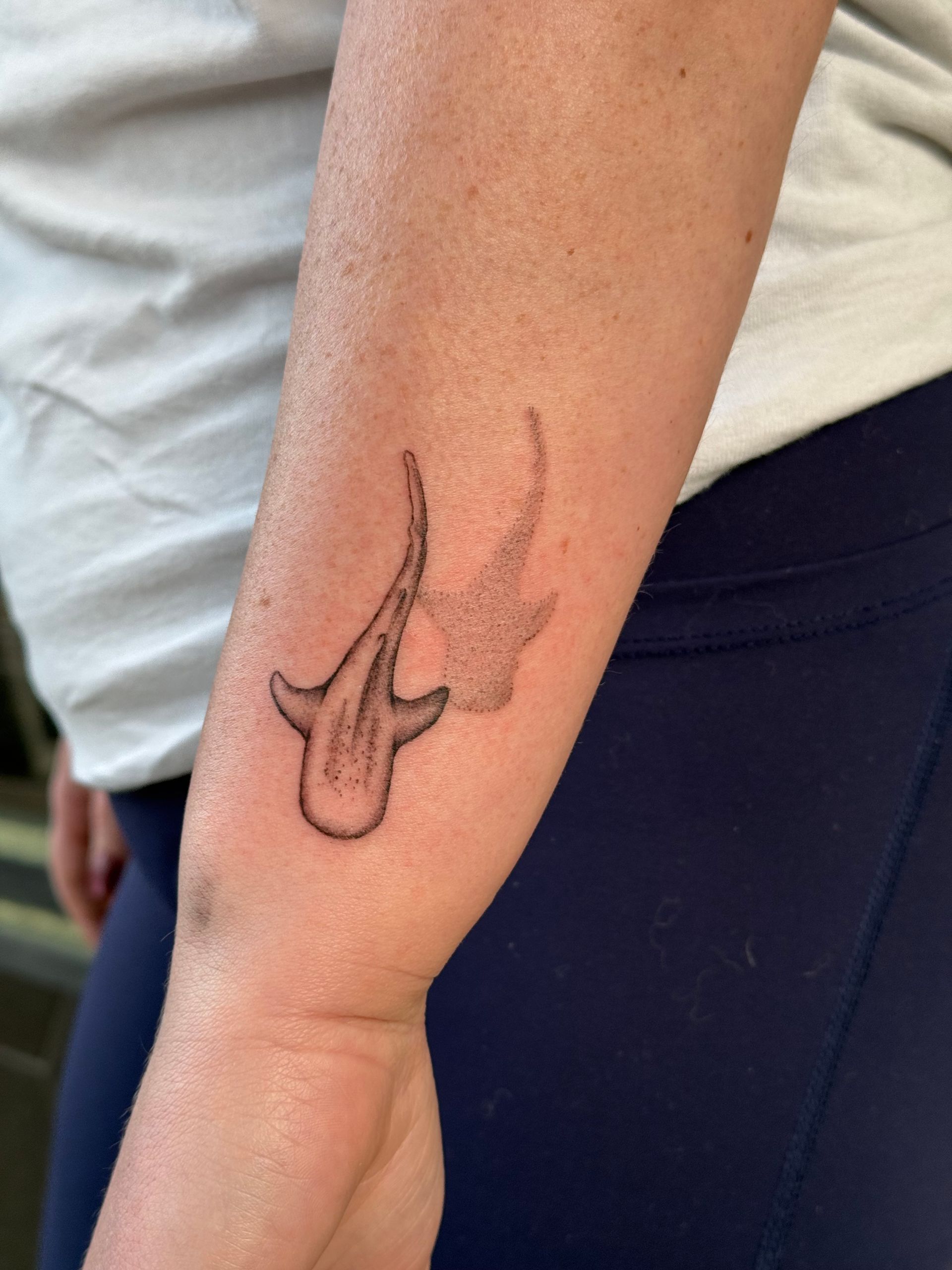 Arm with a dark line-art tattoo of a bird-like figure near the elbow.