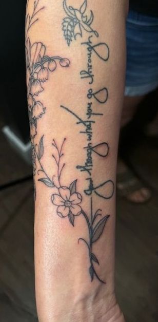 Forearm tattoo of a vertical vine with flowers and cursive writing in black ink