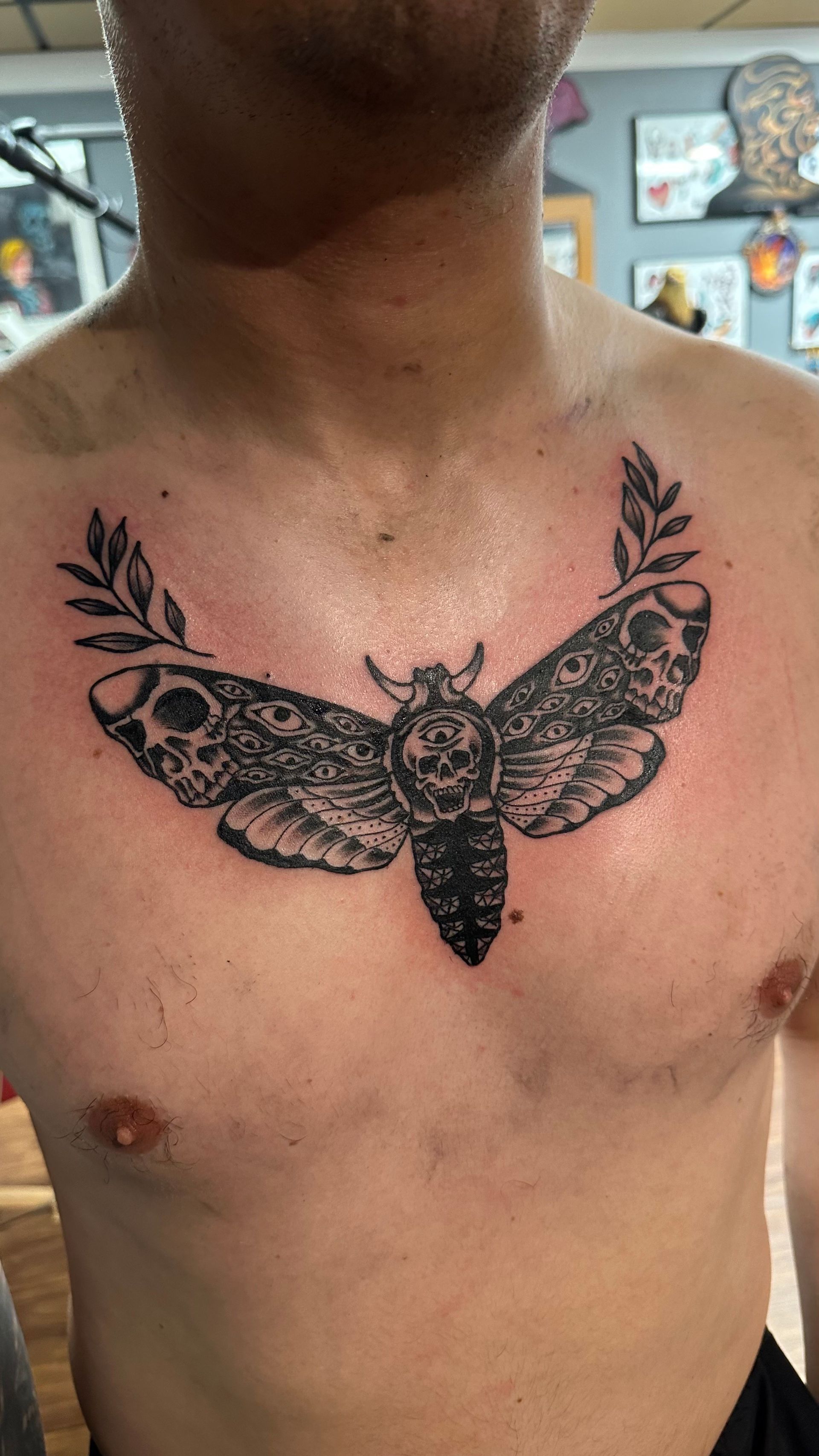 Close-up of a chest tattoo featuring a detailed black moth or butterfly with floral wing patterns