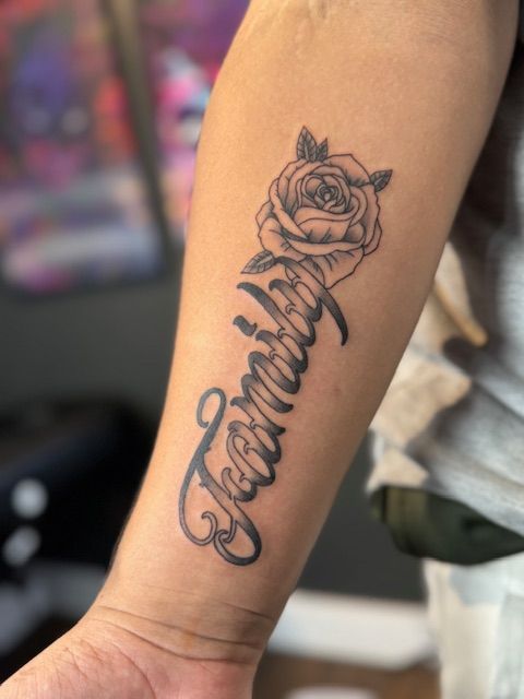 Forearm tattoo with a rose above cursive script reading “beautiful”