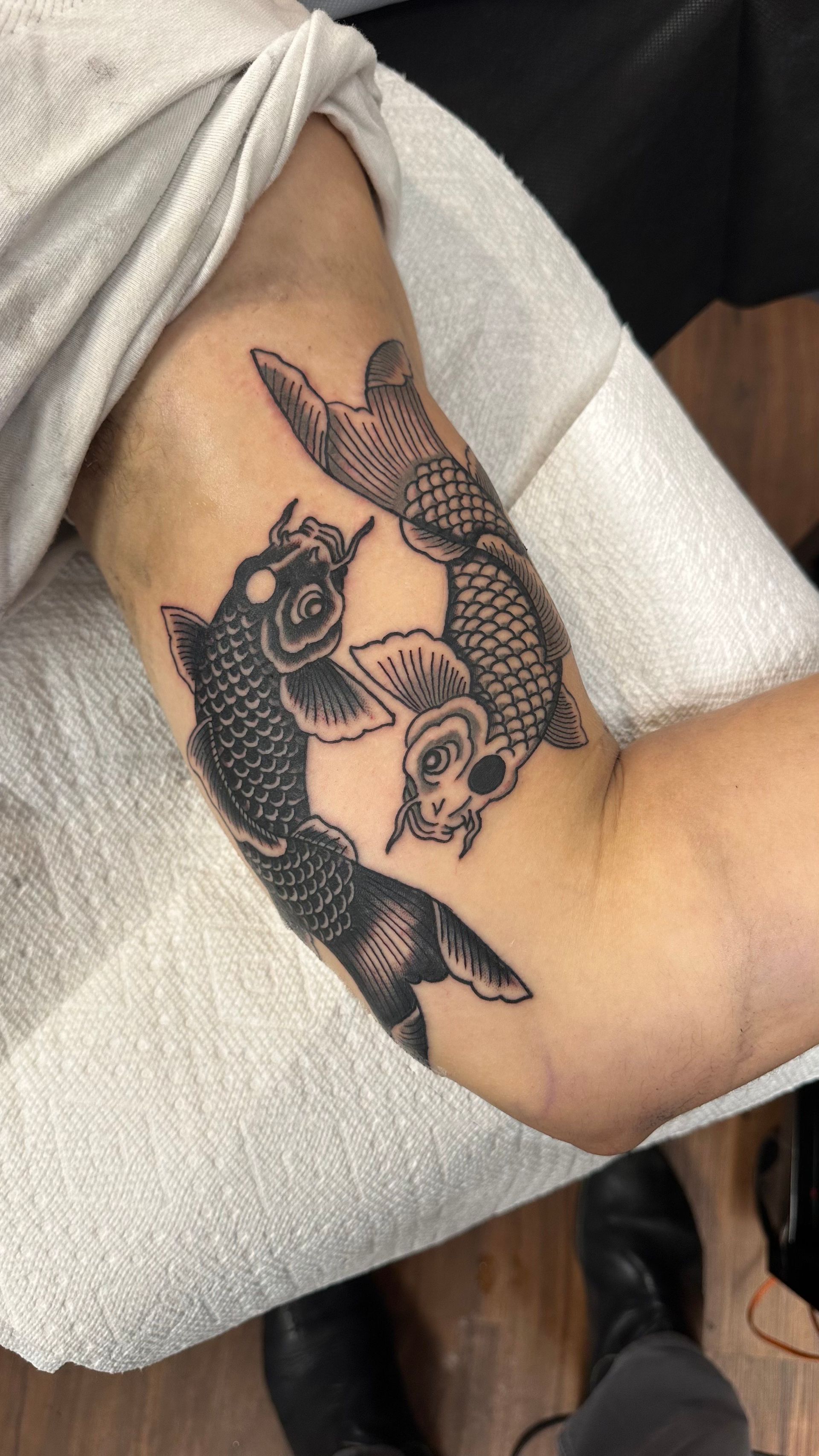 Arm tattoo with two black koi fish on a bent arm, resting on a white towel.