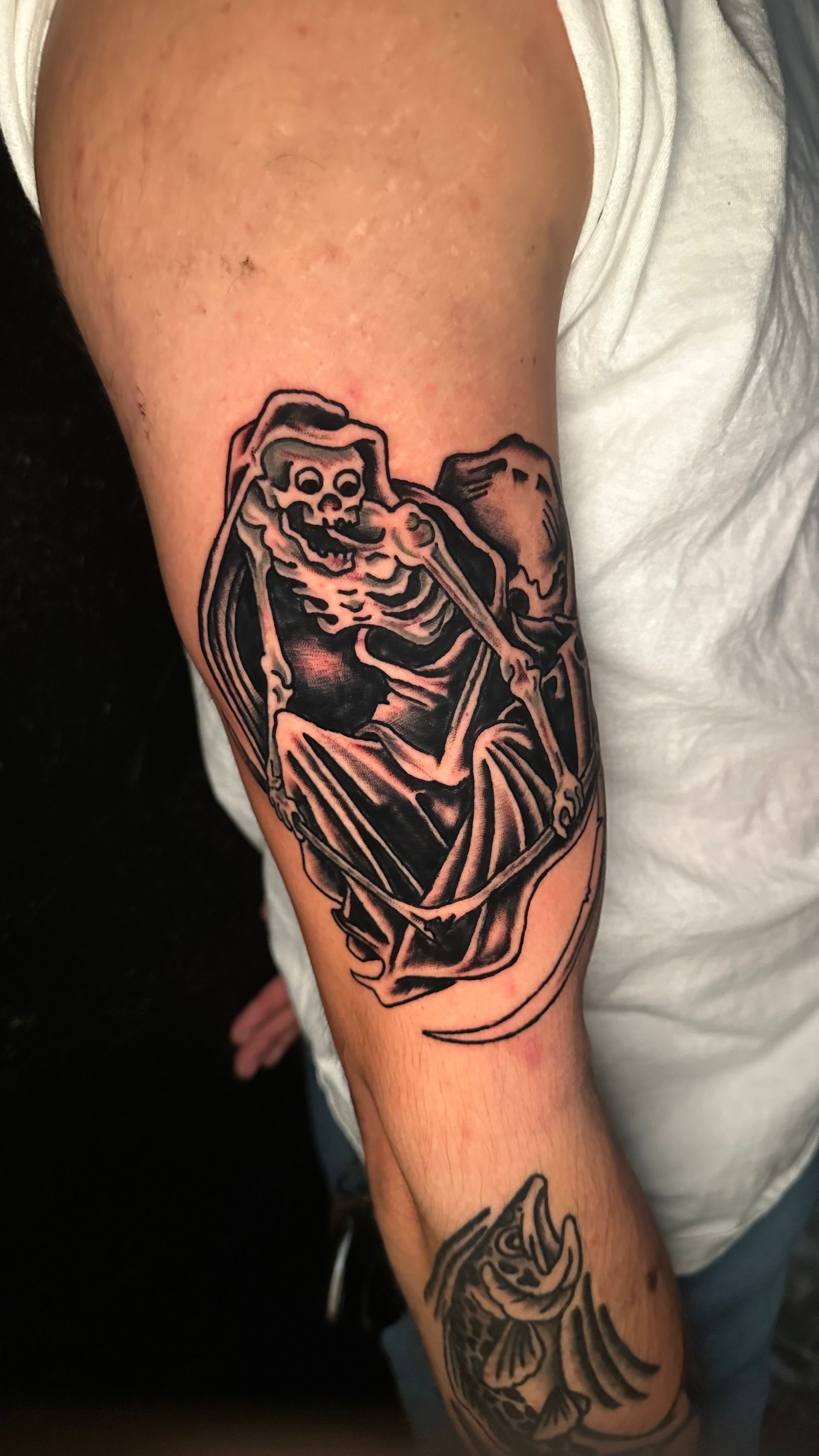 Close-up of an arm with a black-and-gray tattoo of a hooded skeleton figure
