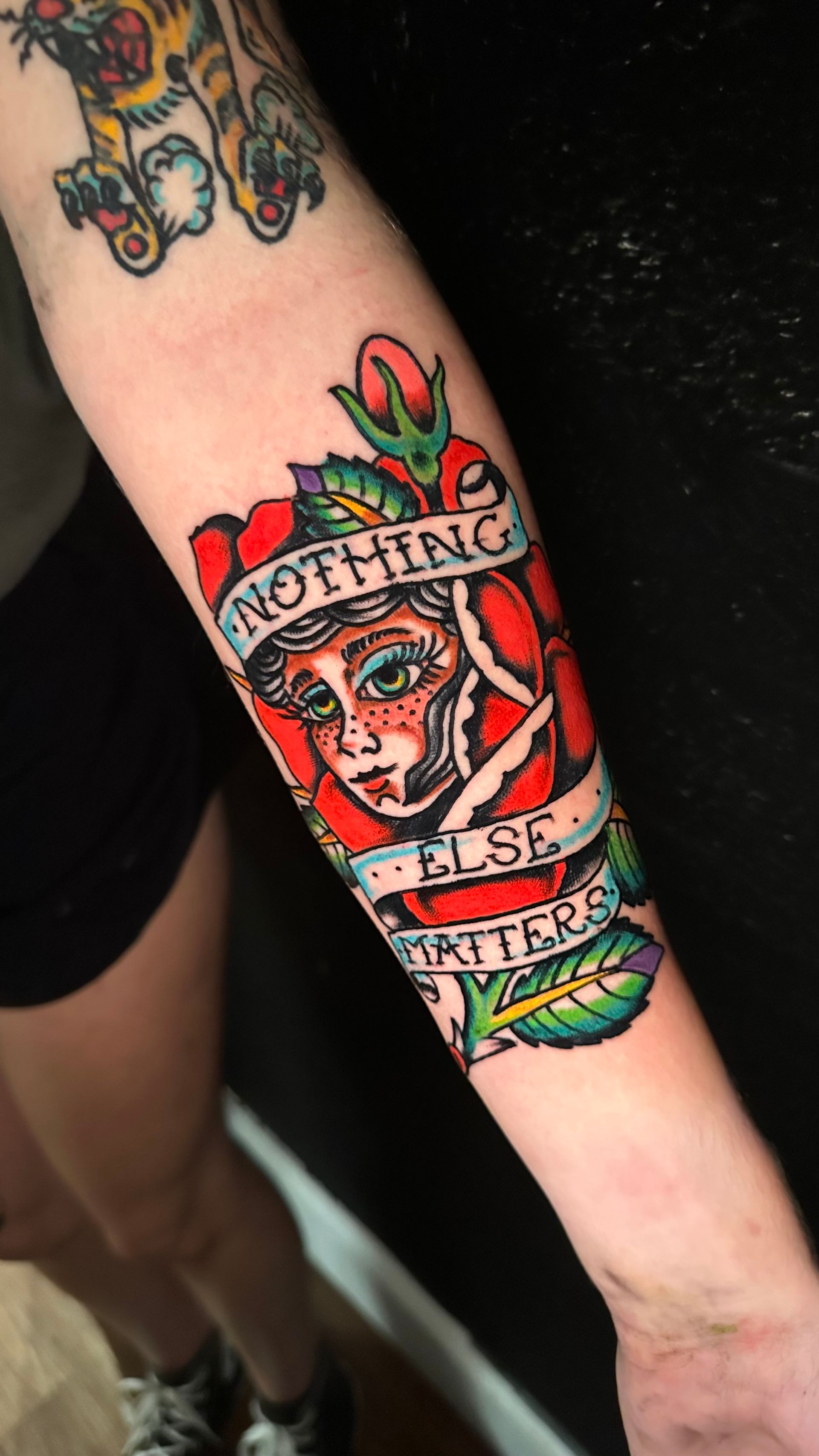 Forearm tattoo of a red skull with roses and a banner reading “Nothing else matters”