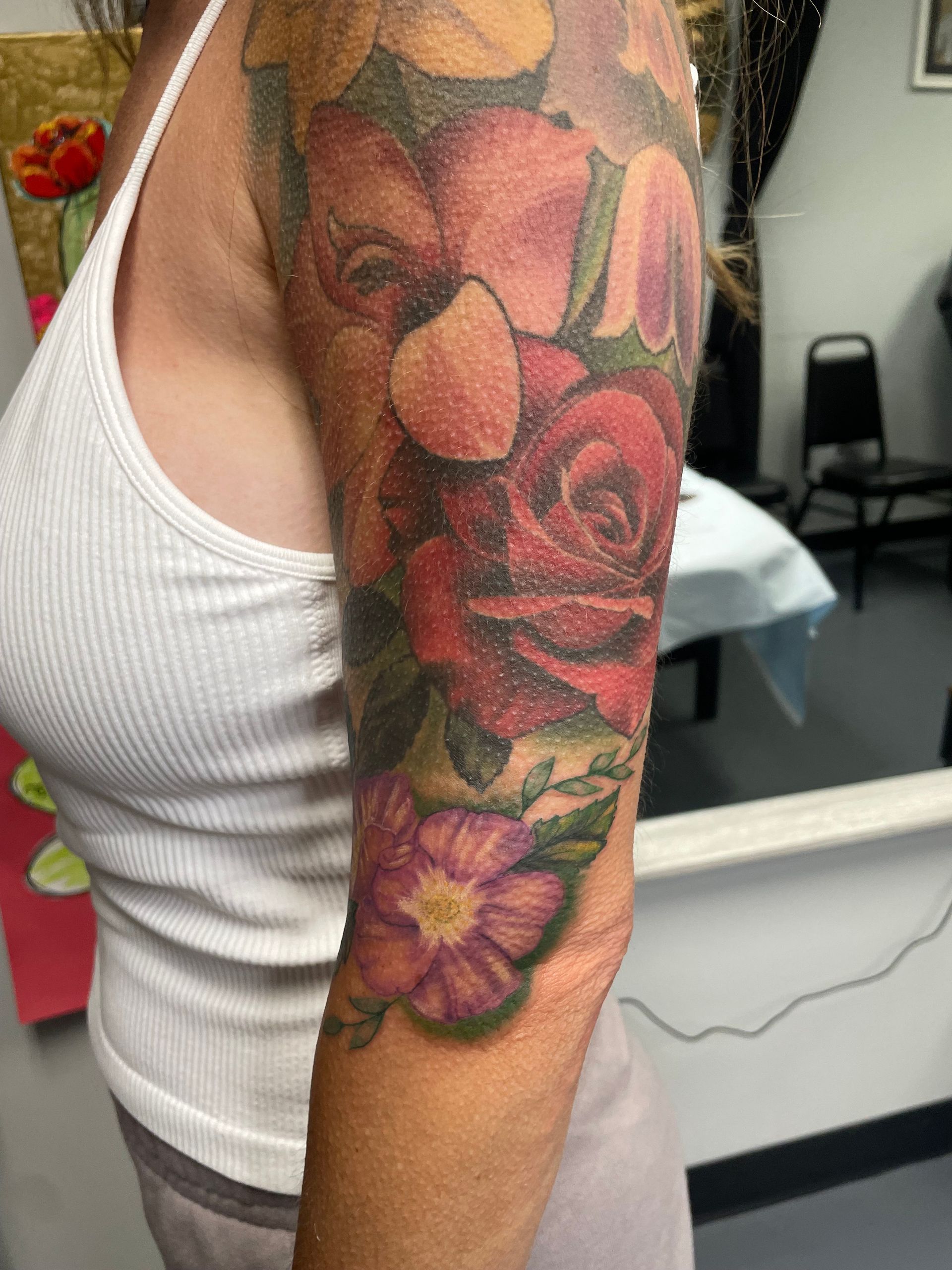 Close-up of an arm with a colorful floral tattoo sleeve, showing pink and purple flowers.