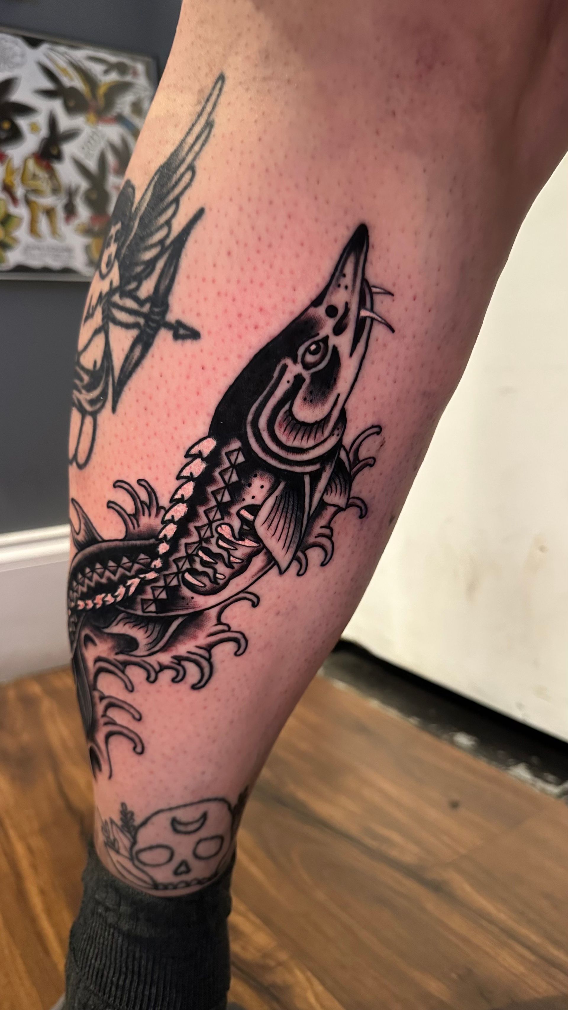 Black-and-gray fish tattoo on a person's calf, with a partial tattoo visible above and below it.
