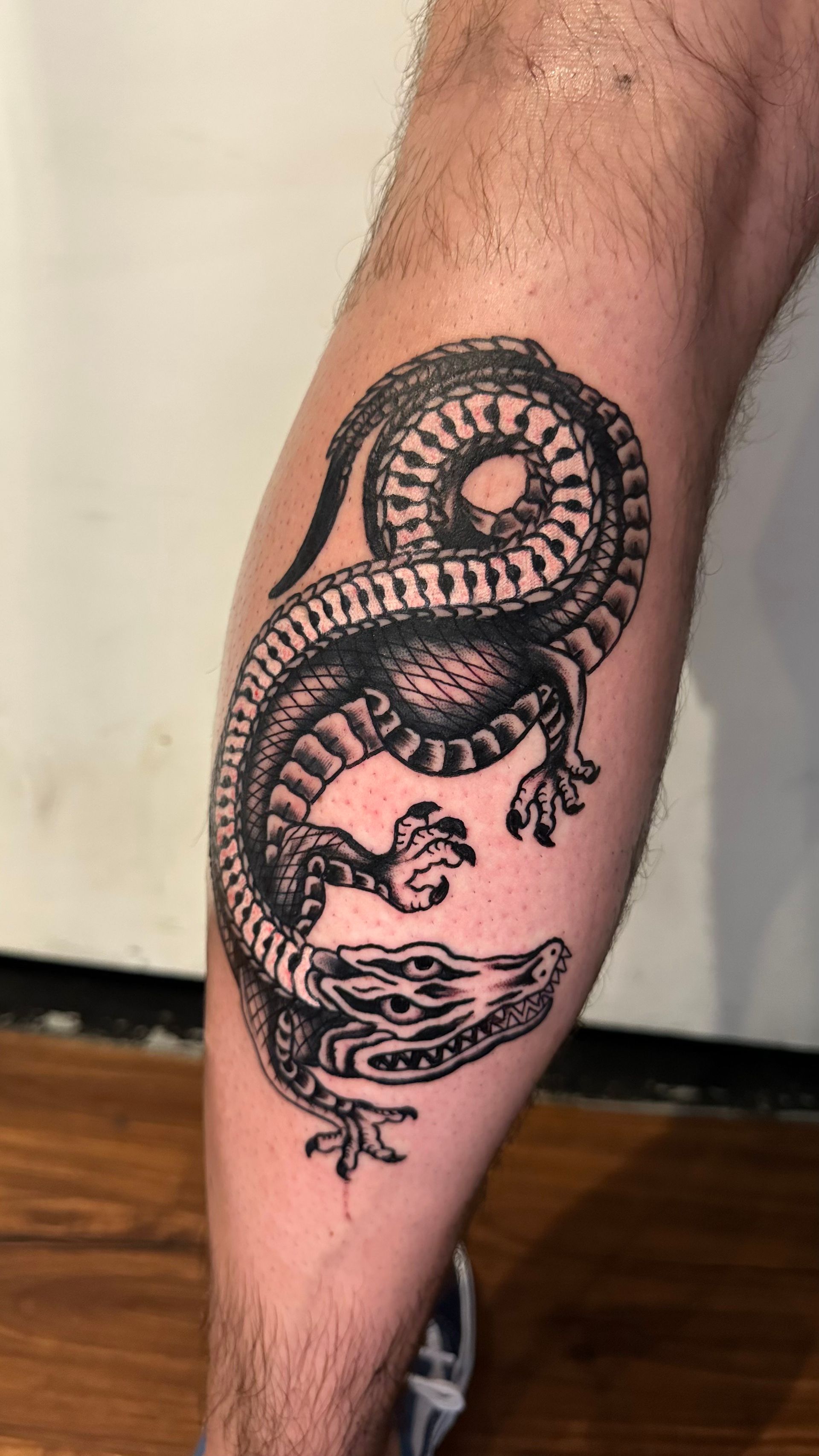 Black snake tattoo coiled around a leg calf, with a fish below on skin background