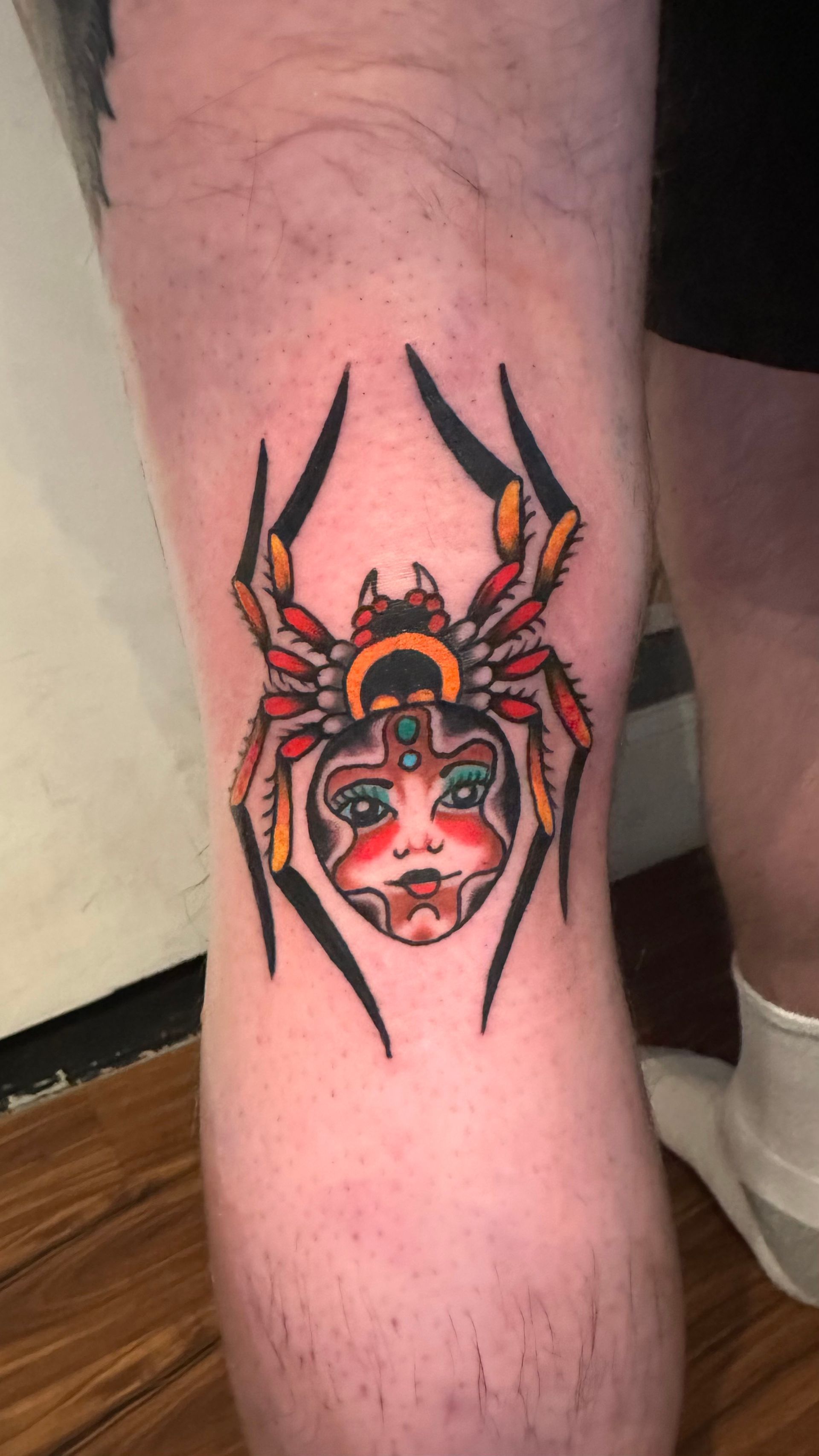 Colorful horned mask tattoo with black spikes on a person’s lower leg