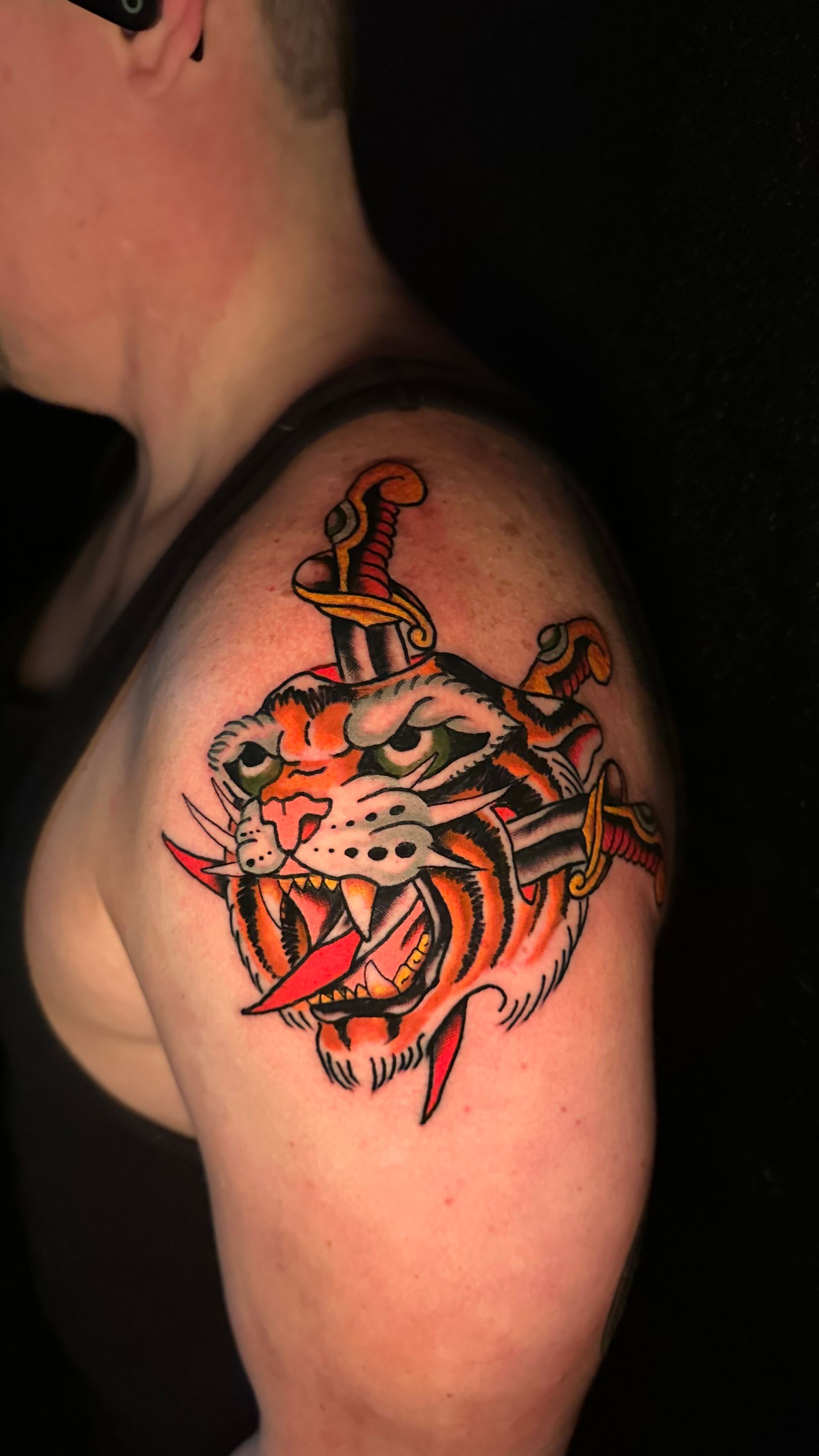 Arm tattoo of a snarling tiger with a sword, in bold red, black, and orange ink
