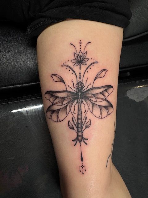 Black butterfly tattoo on a person's calf with symmetrical floral and dot details.