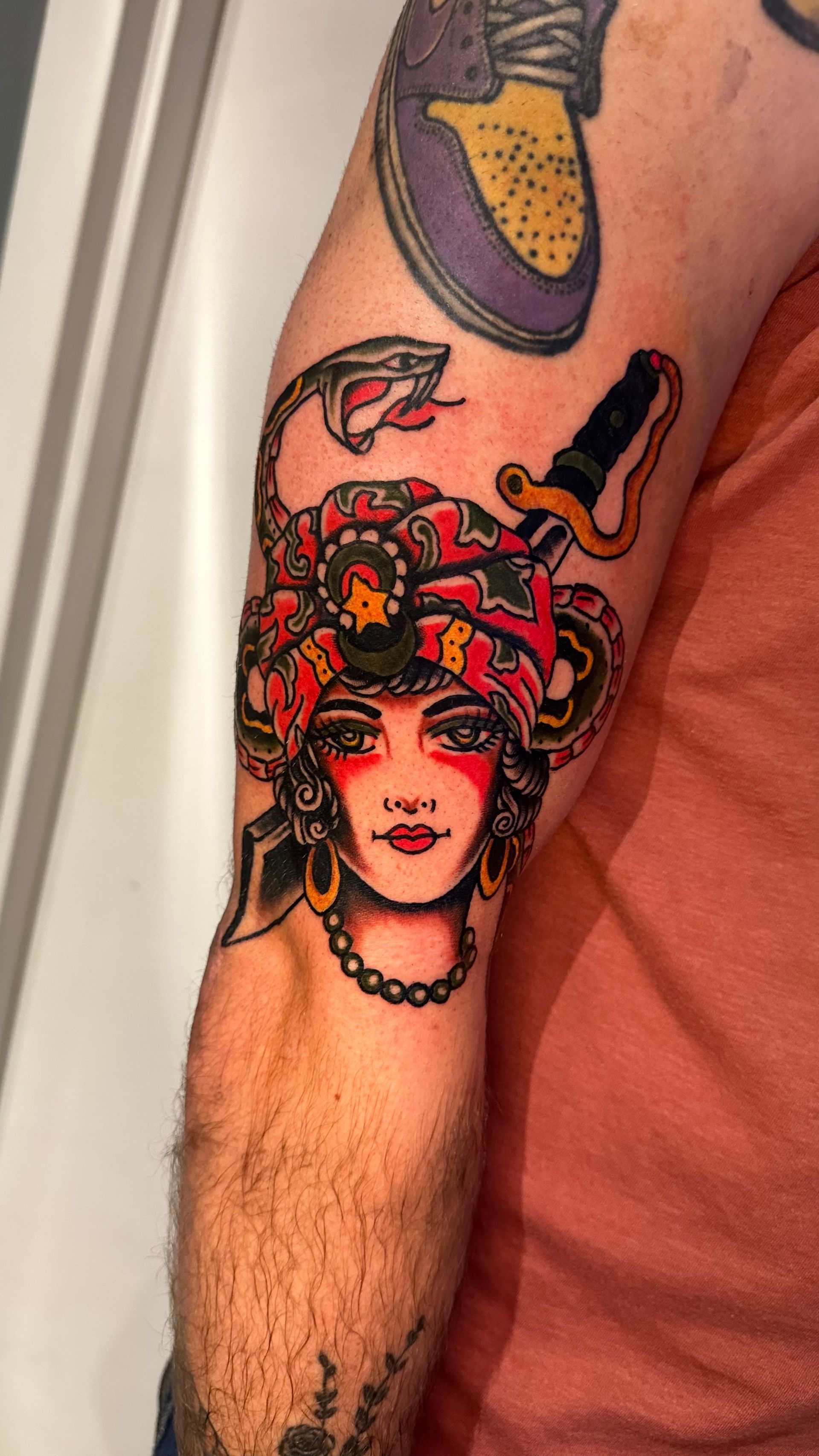 Arm tattoo of a colorful woman’s face with a snake and floral headdress on a forearm