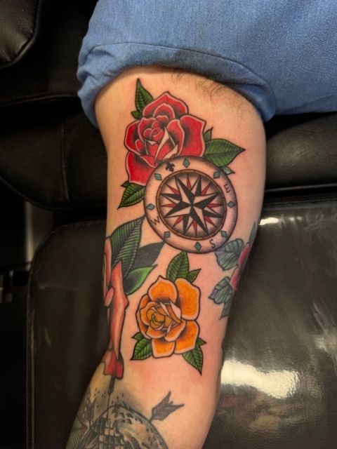 Forearm tattoo with red and yellow roses, green leaves, and a compass design