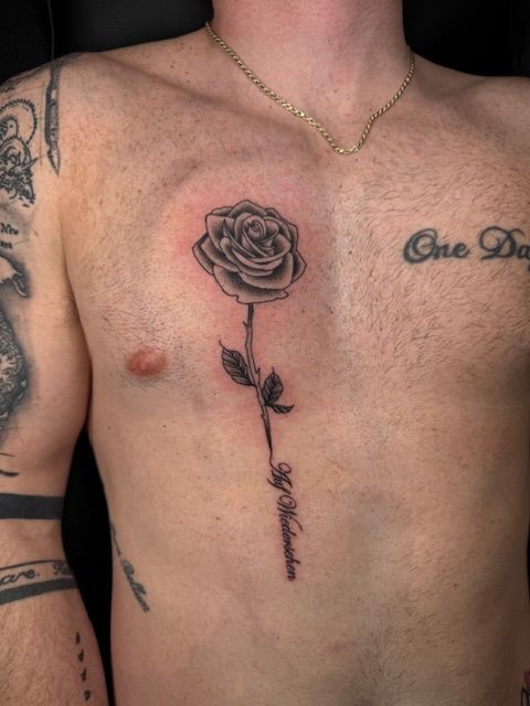 Close-up of a shirtless torso with a black rose tattoo down the center of the chest.