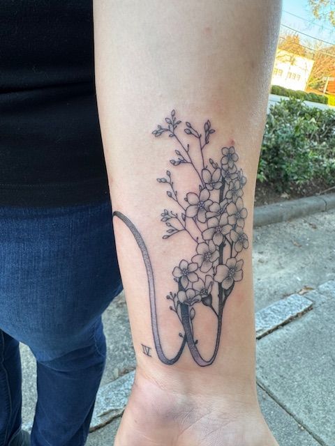 Ankle tattoo of a floral bouquet with a long looping stem on a leg outdoors.
