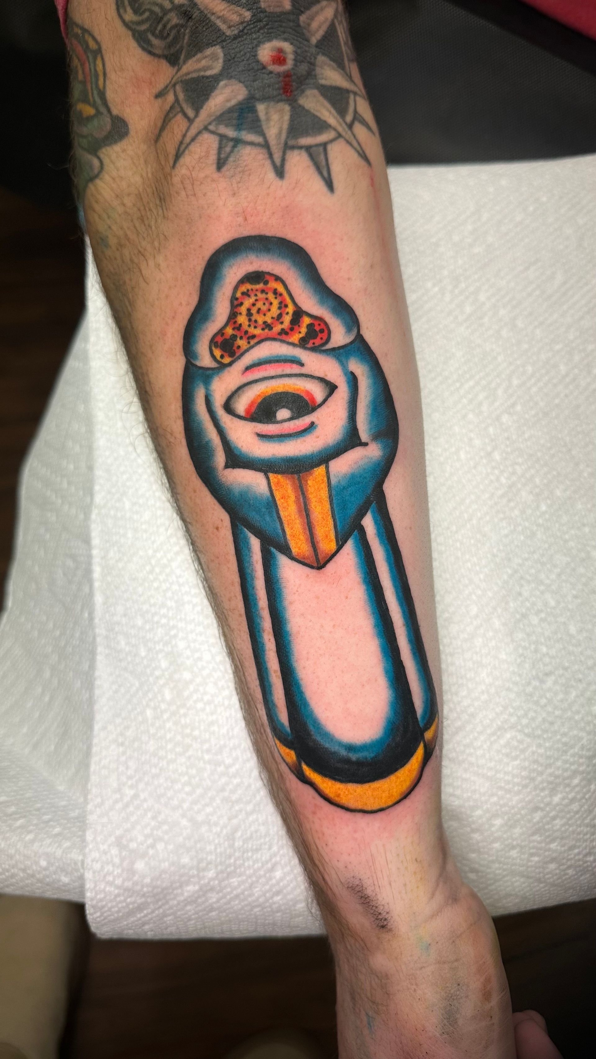 A colorful tattoo of a stylized eye on a leg, with orange, blue, and pink outlined details.
