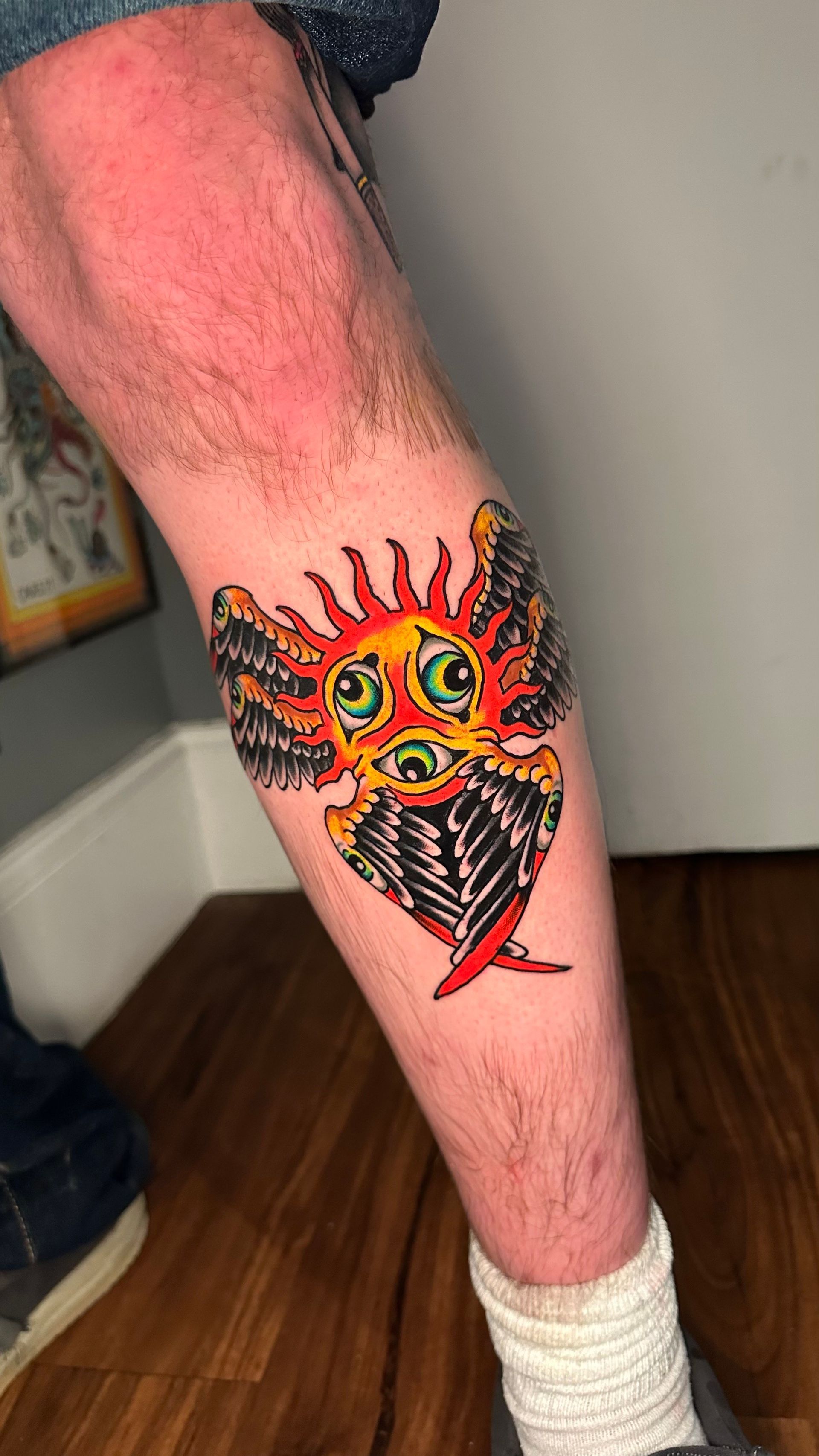 Lower leg with a colorful fiery eye tattoo on the calf, wearing a white ankle wrap.