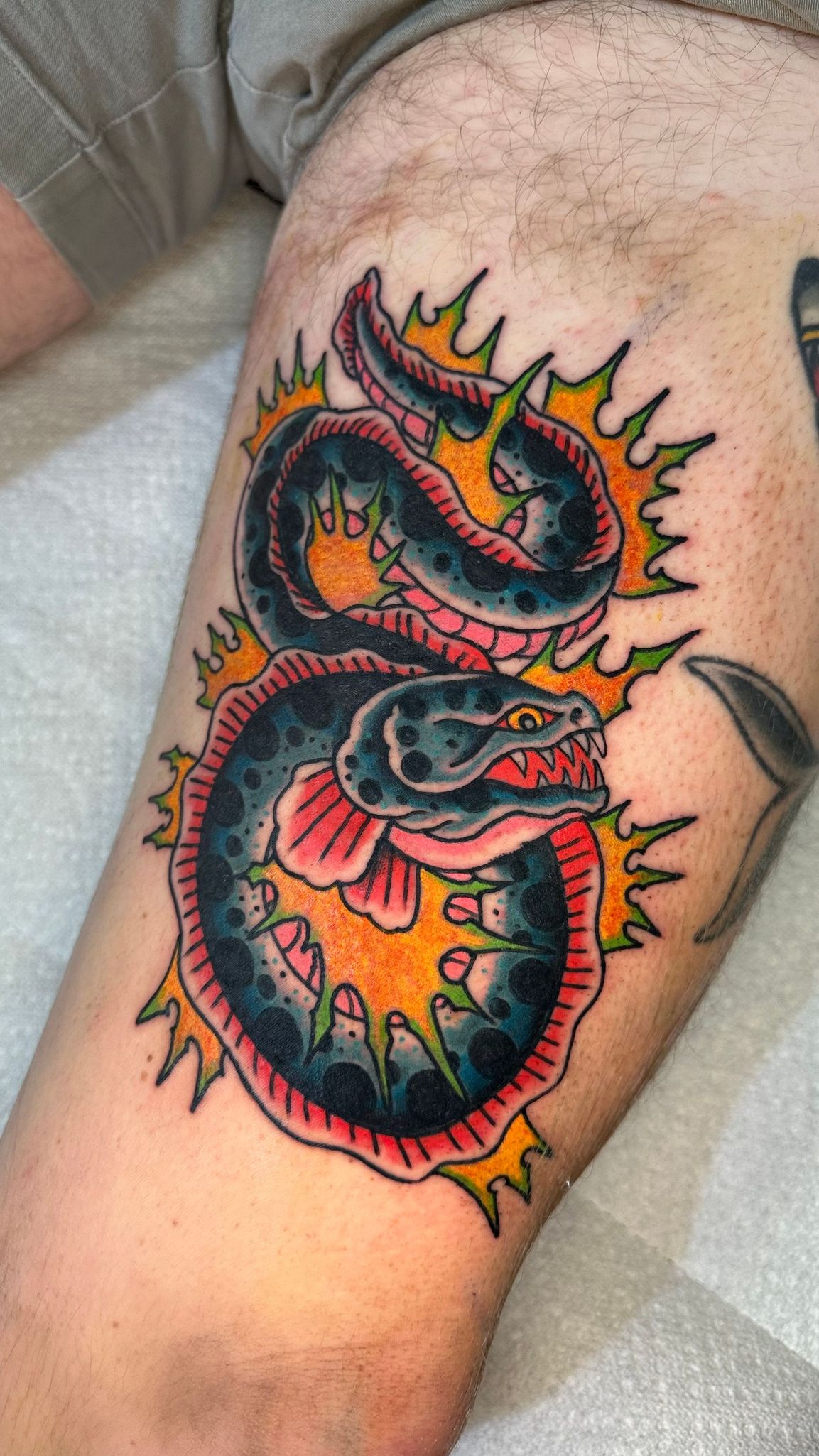 Colorful coiled snake tattoo with orange flames on a person's upper arm
