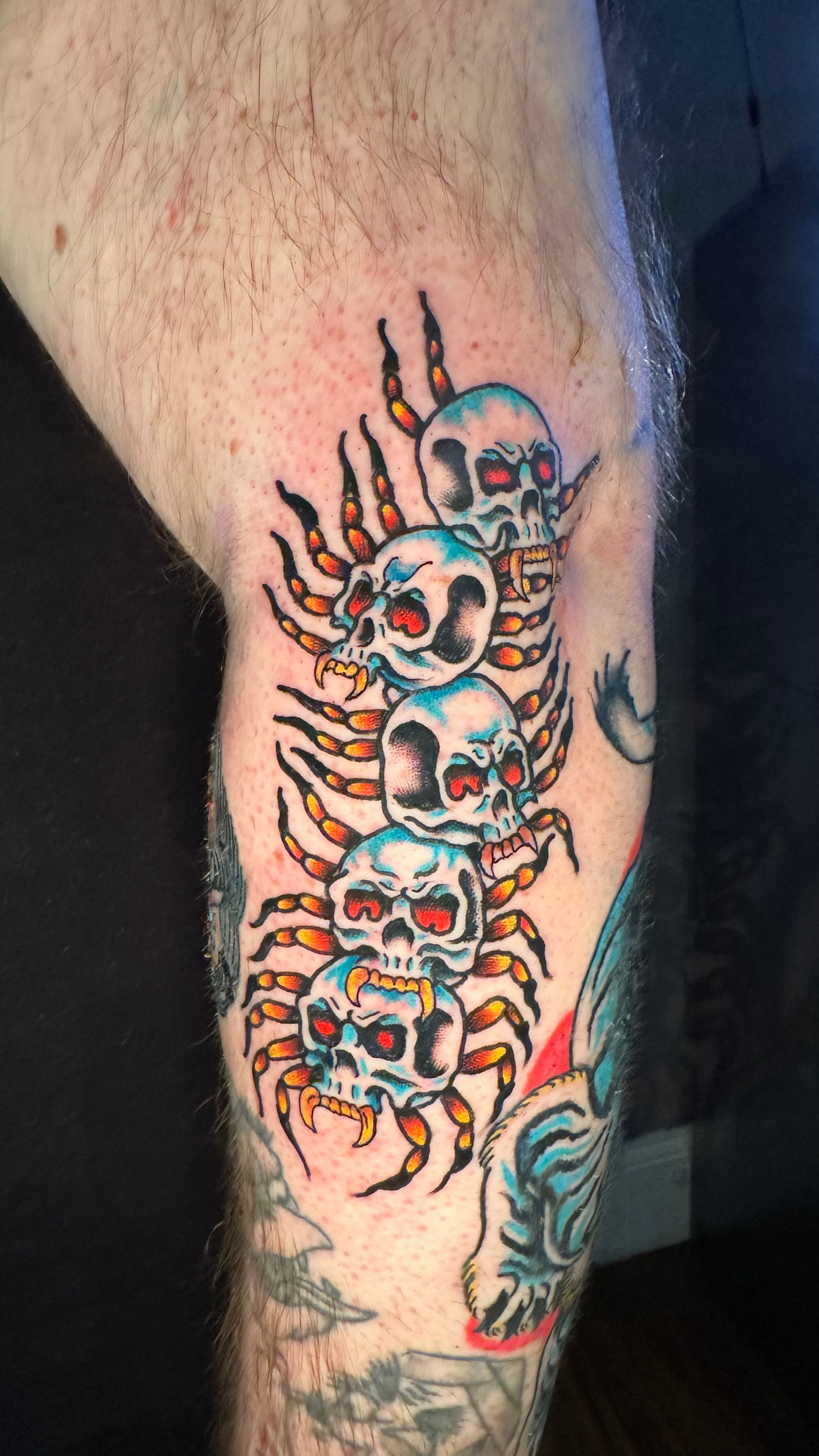 Colorful tattoo of stacked skulls with red and blue accents on a person's leg