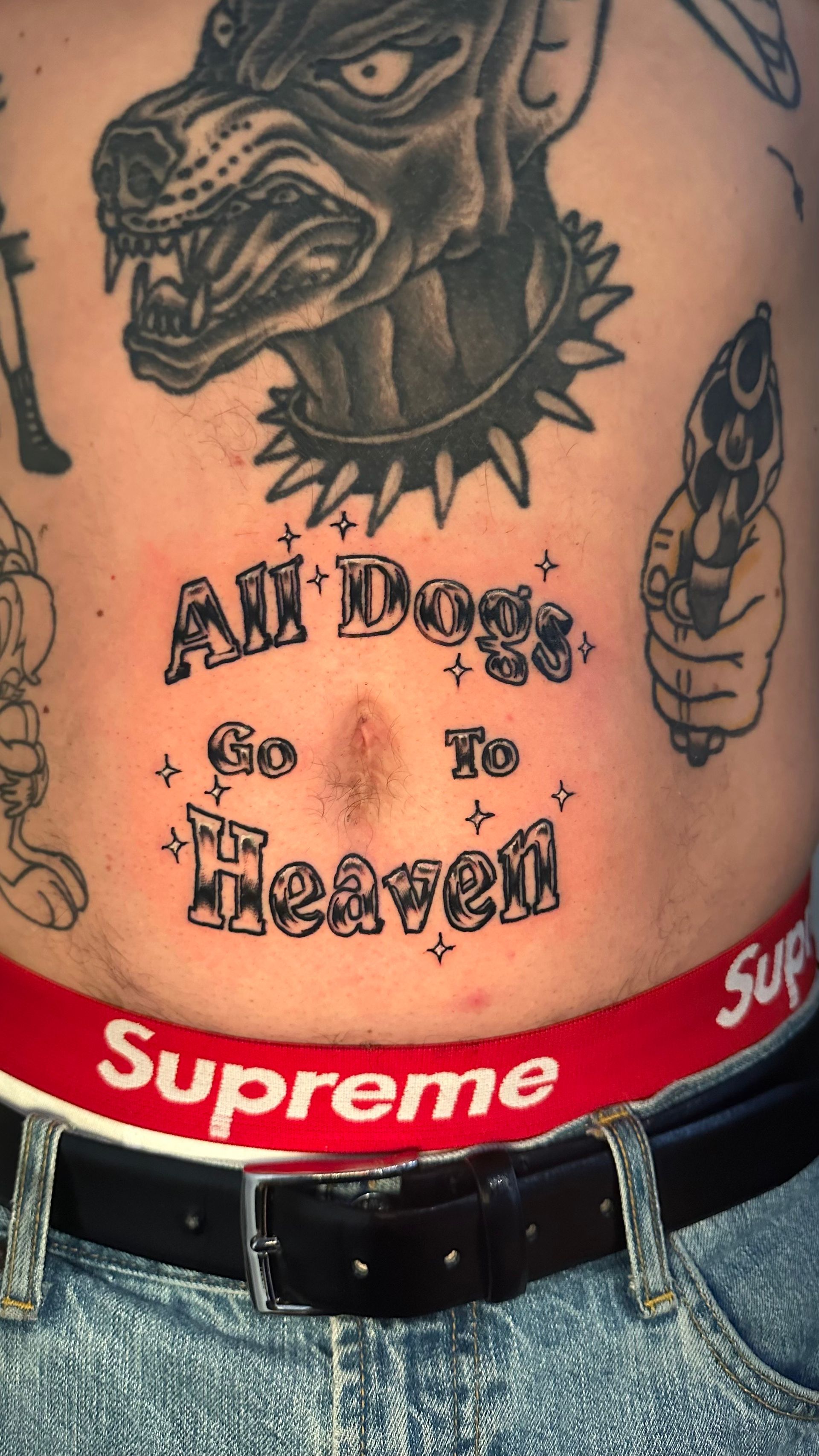 Torso tattoo with a dog and the text “All Dogs Go to Heaven” above red Supreme underwear band