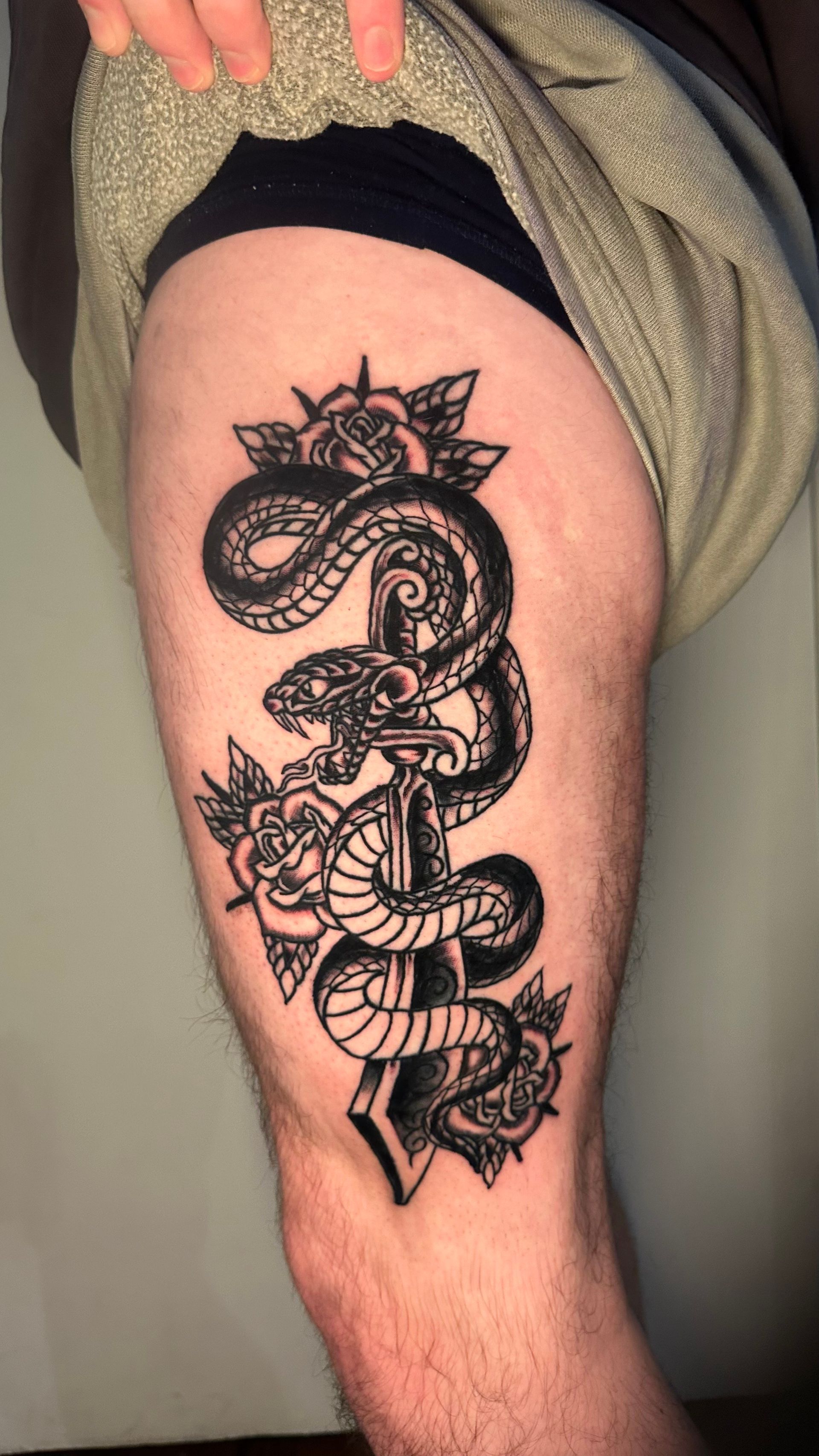Black snake tattoo on a thigh, with ornate linework and small decorative shapes around it