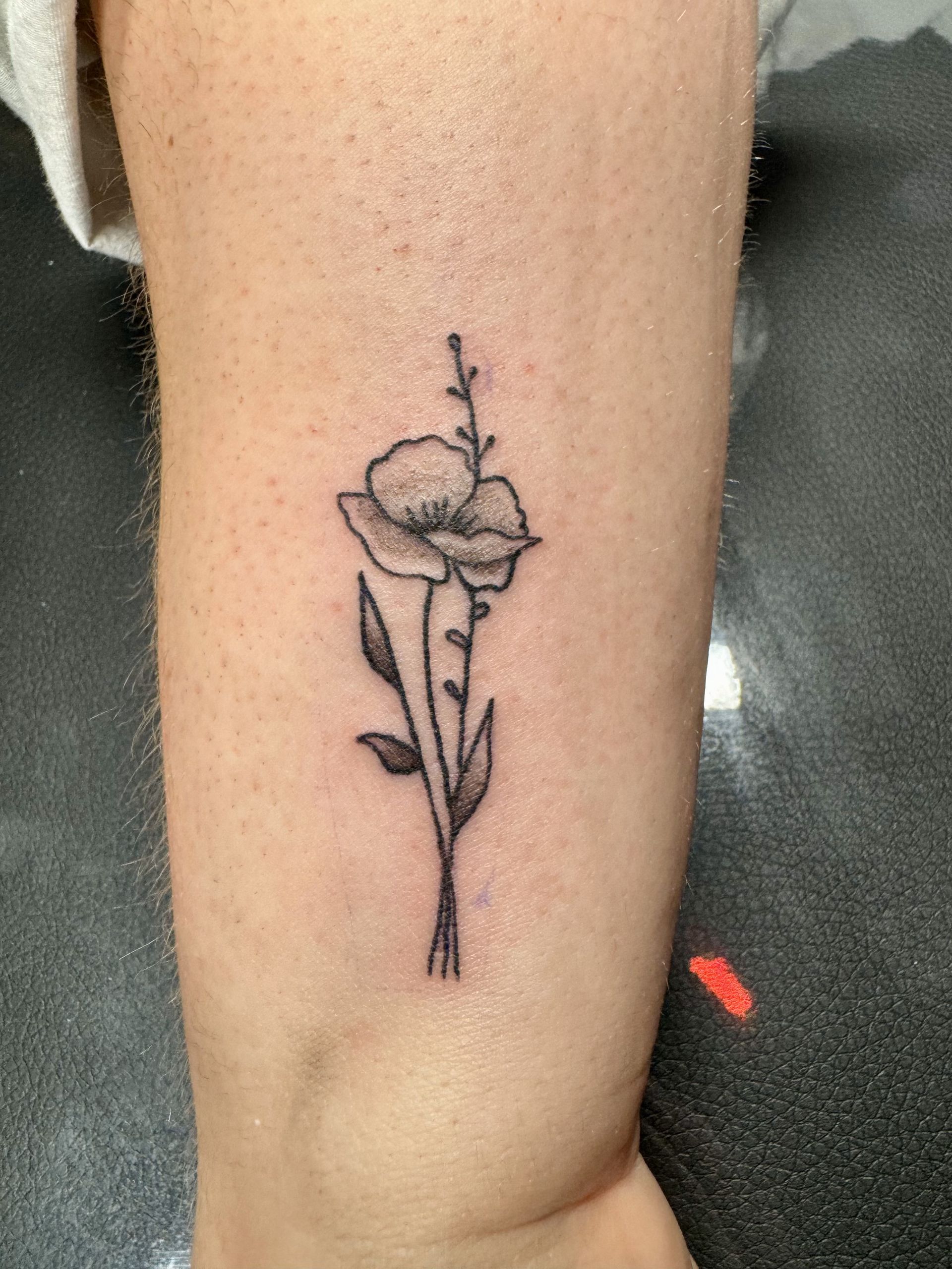 Small black line-art flower tattoo on a person’s forearm near the elbow.