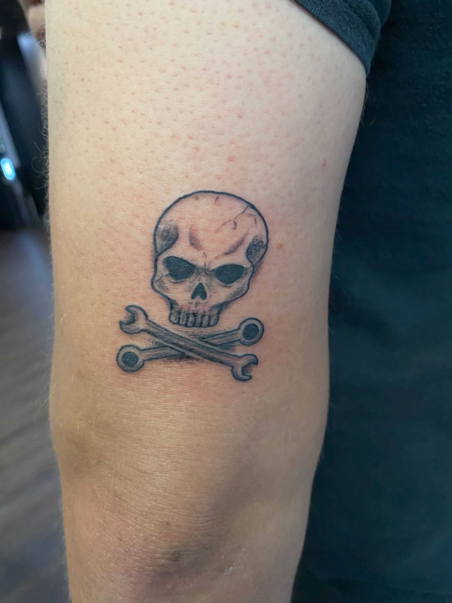 Close-up of a black skull and crossbones tattoo on a forearm.