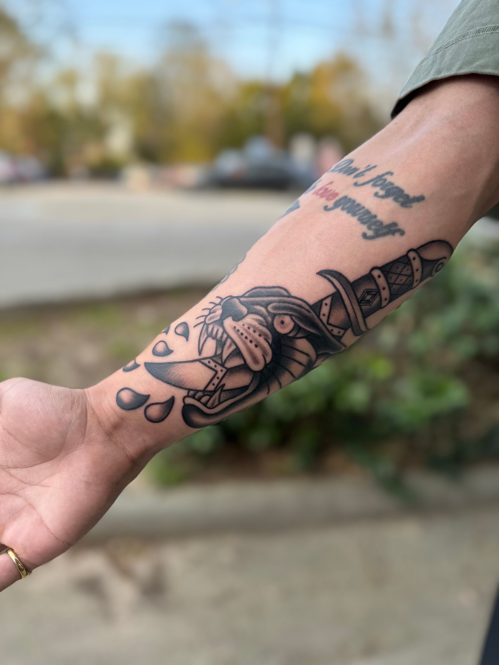 Forearm with black linework tattoos, including a rose and face, outdoors with a blurred background