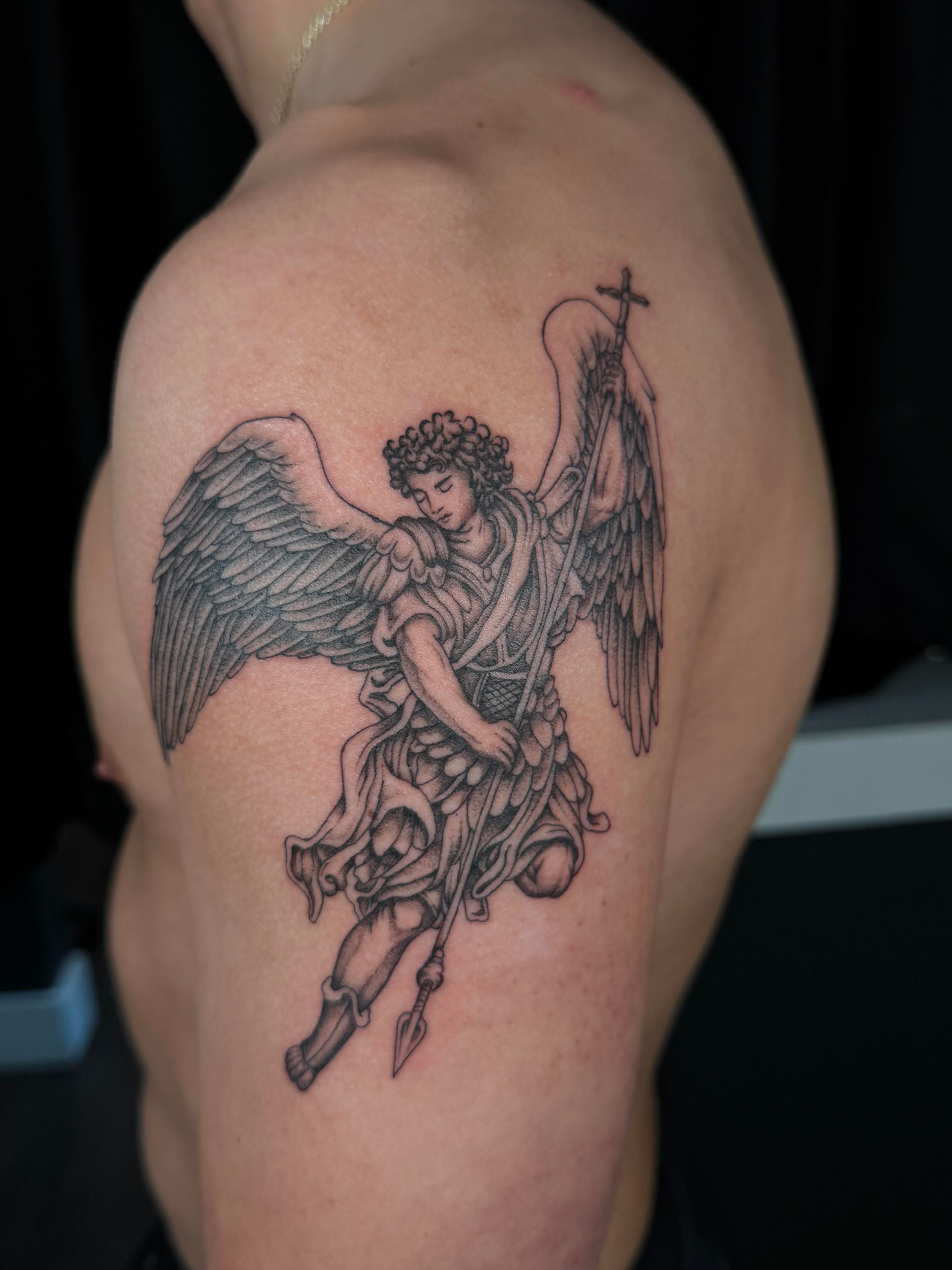 Black-and-gray angel tattoo on an upper arm, with one wing dark and the other outlined in red.