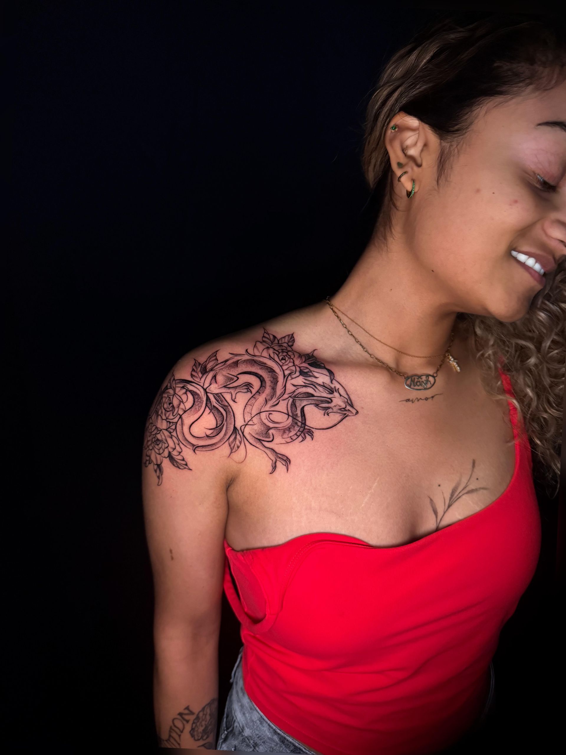 Smiling woman in red strapless top with floral shoulder tattoo against a black background