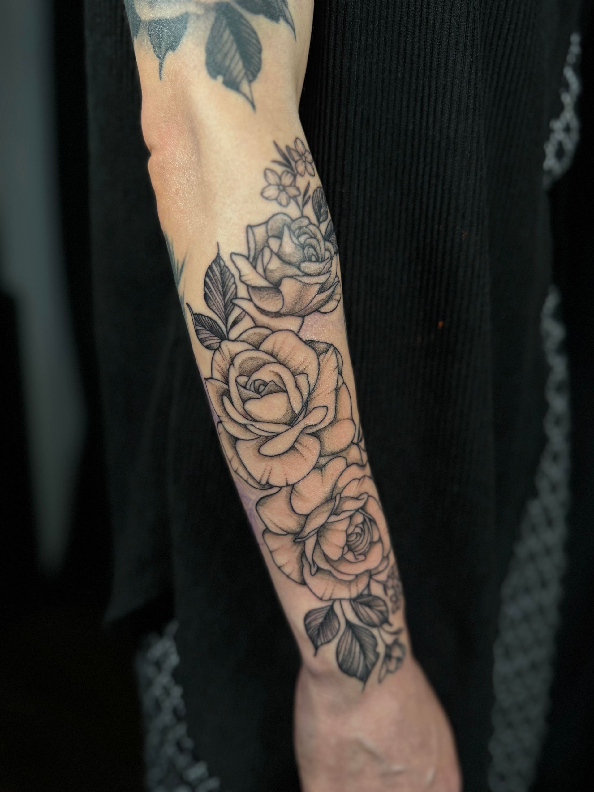 Tattooed forearm with black-and-gray floral rose design against a dark background