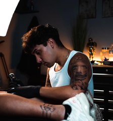 Tattoo artist working on a client in a dim studio, with warm lamp lighting and tools nearby