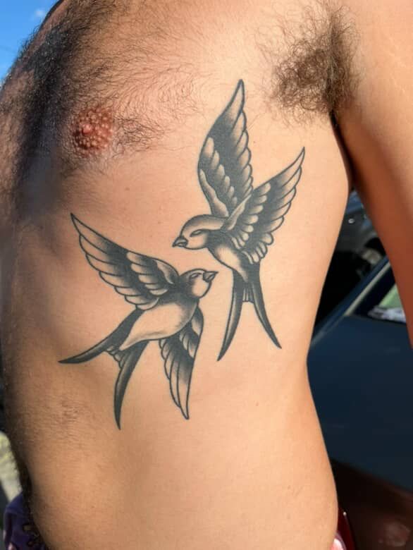 Black bird tattoo on a person’s side, with two birds in flight on bare skin