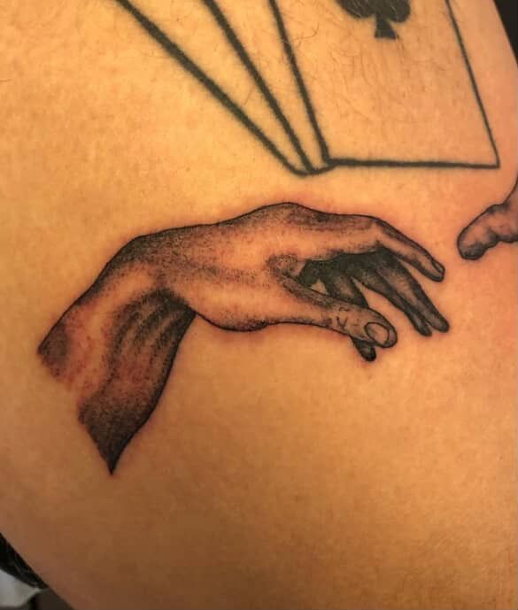 Black-and-gray tattoo of a hand reaching downward on skin