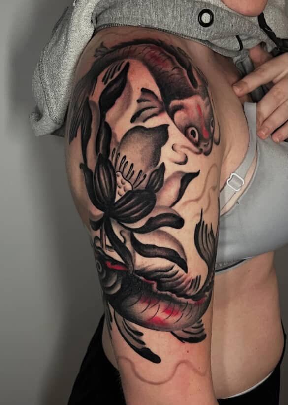 Arm tattoo of a koi fish and floral design in black and red ink on an upper arm