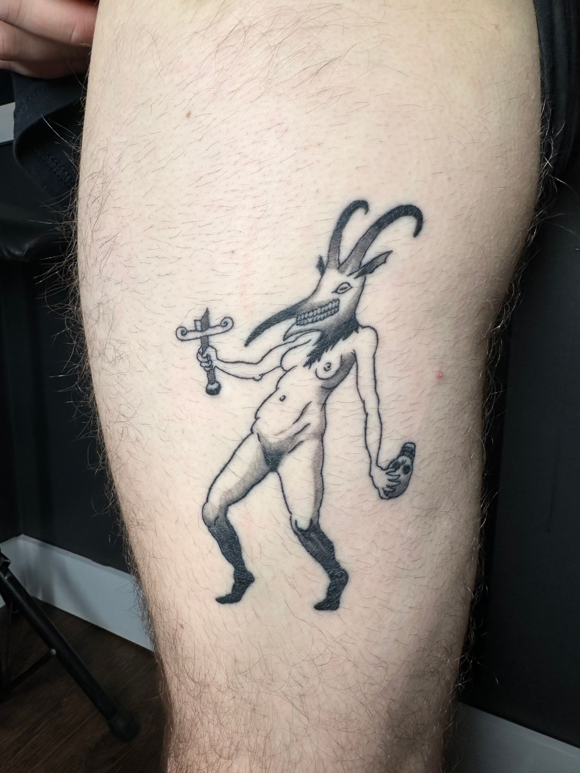 Black-and-white tattoo of a horned, long-limbed cartoon creature on a person’s leg